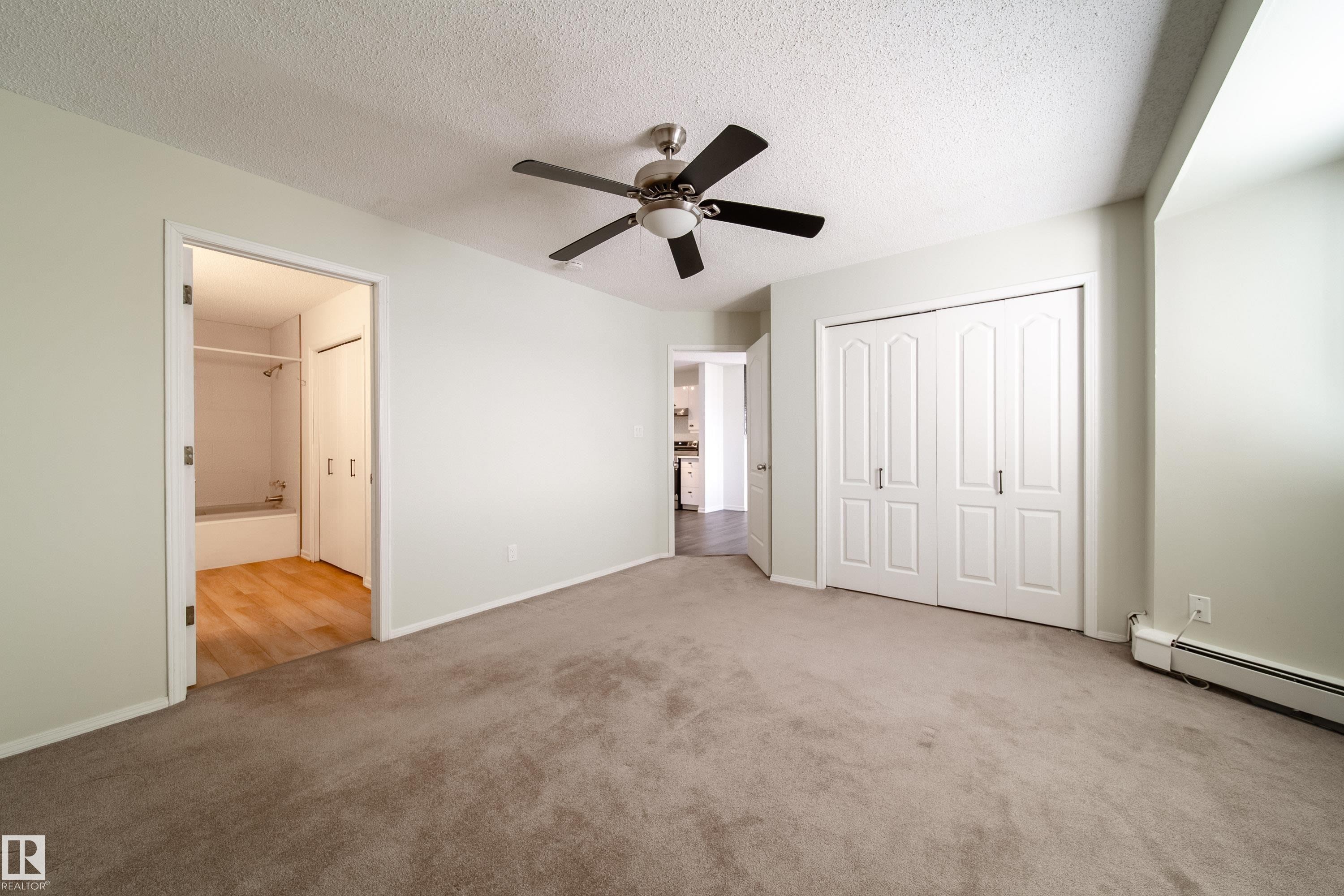 Carpeted interior space featuring a ceiling fan, light-colored walls, and a double-door closet with panel detailing - 302 9138 83 Avenue, Edmonton, AB - Indoor Photo Showing Other Room