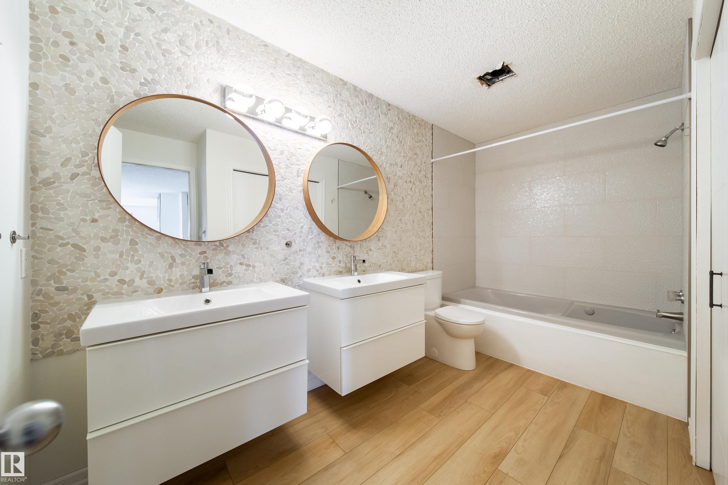 Bathroom featuring wood-finish flooring and a stone pebble accent wall - 302 9138 83 Avenue, Edmonton, AB - Indoor Photo Showing Bathroom
