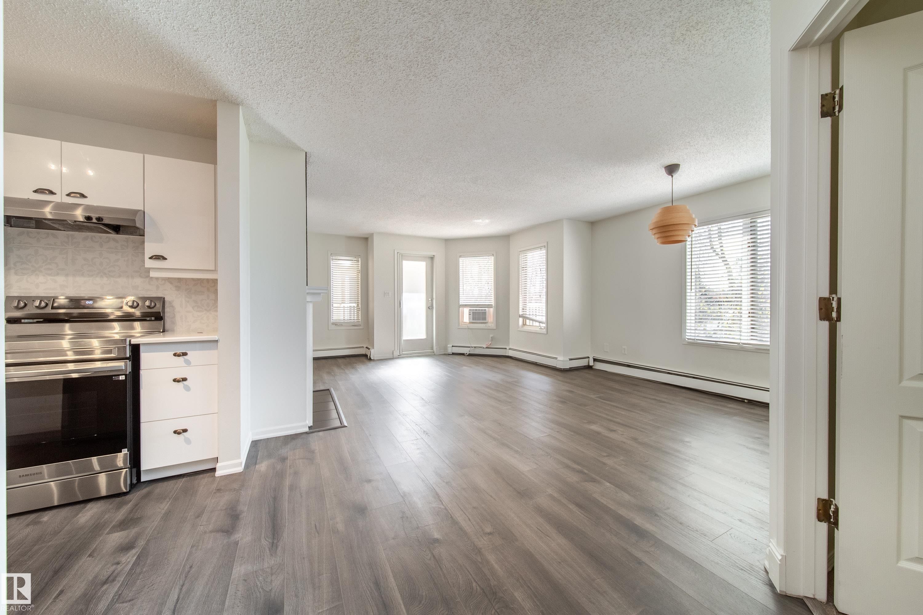 Open-concept living area featuring wood-finish flooring, white walls, and a modern pendant light fixture - 302 9138 83 Avenue, Edmonton, AB - Indoor Photo Showing Kitchen