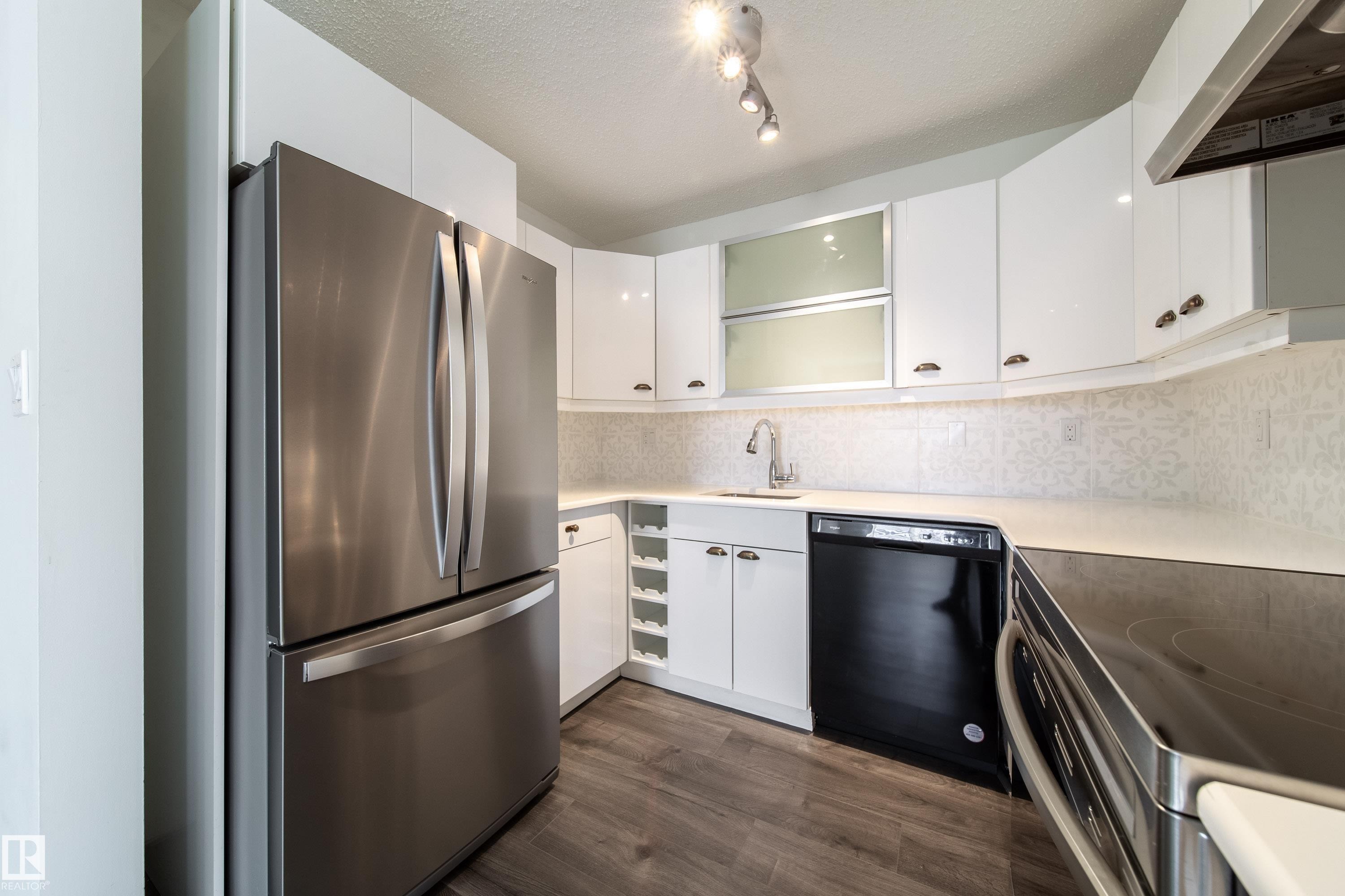 Modern kitchen featuring stainless steel appliances, white cabinetry, quartz-finish countertops, and wood-finish flooring - 302 9138 83 Avenue, Edmonton, AB - Indoor Photo Showing Kitchen
