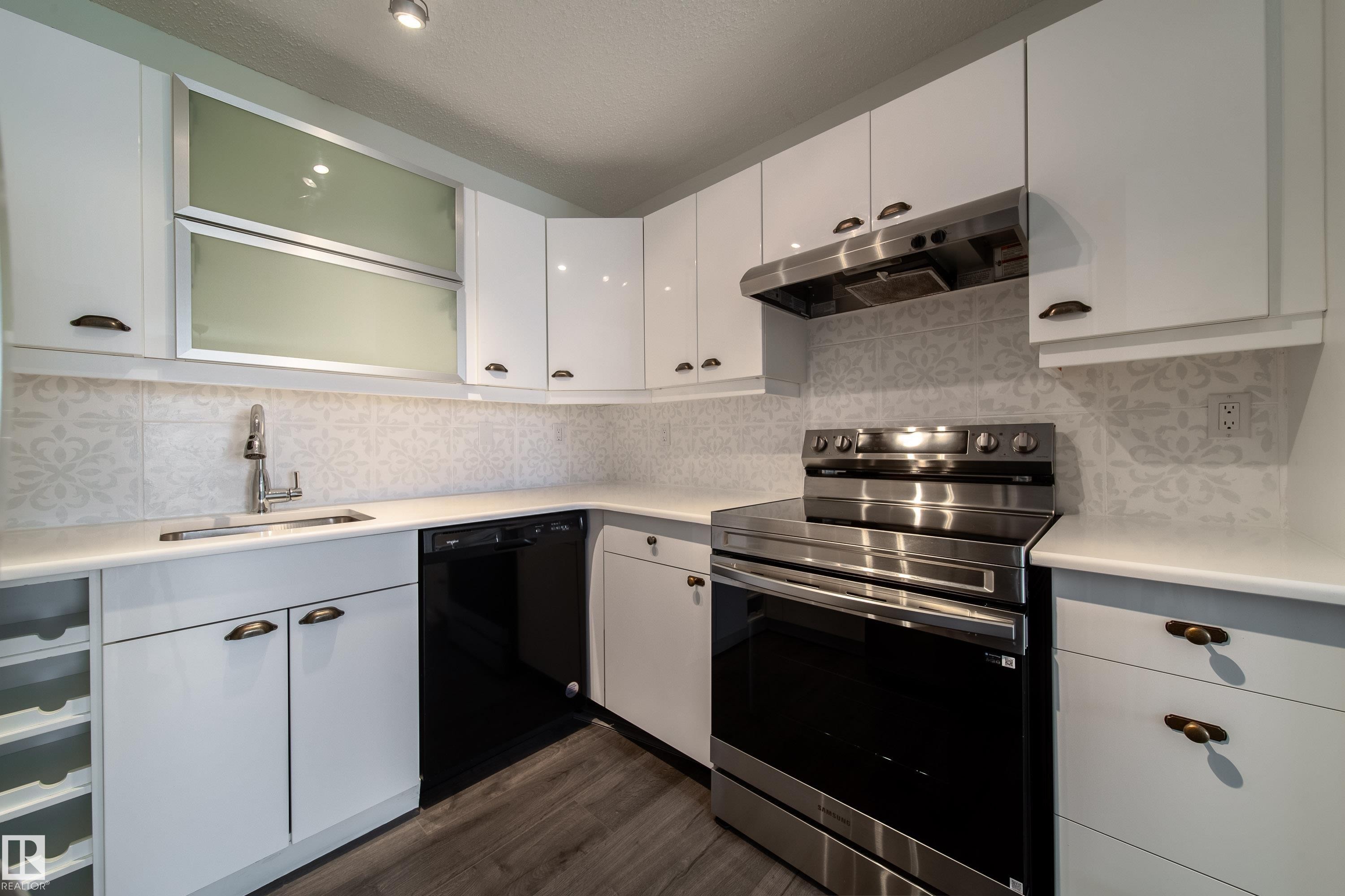 Modern kitchen featuring white cabinetry, stainless steel appliances, a patterned tile backsplash, light-toned countertops, and wood-finish flooring - 302 9138 83 Avenue, Edmonton, AB - Indoor Photo Showing Kitchen