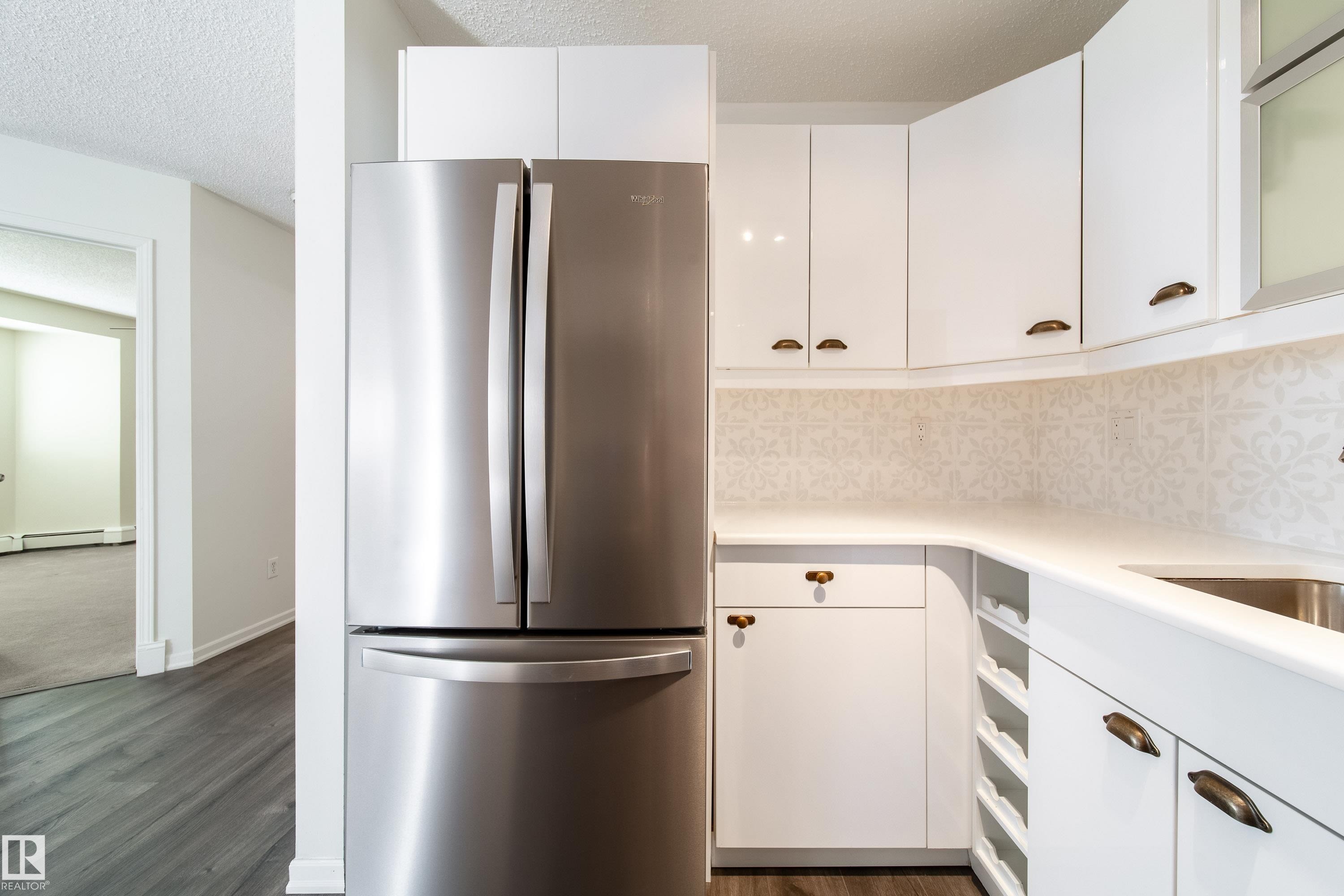 Stainless steel French door refrigerator, white cabinetry with bronze hardware, light-toned countertop, and patterned backsplash tile - 302 9138 83 Avenue, Edmonton, AB - Indoor Photo Showing Kitchen