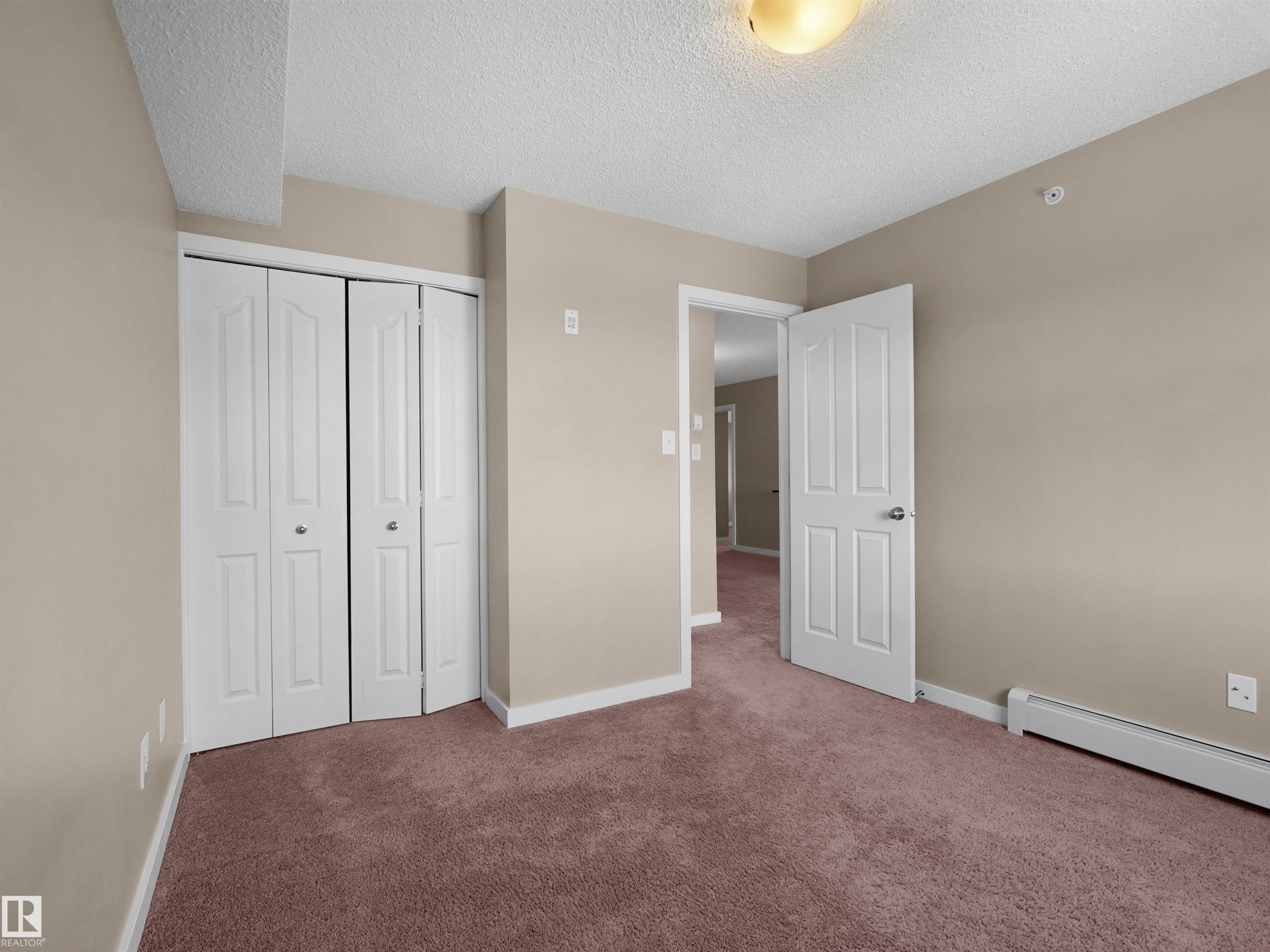 Carpeted room featuring a double bi-fold closet, neutral painted walls, white trim, and a ceiling-mounted light fixture - 417 1060 Mcconachie Boulevard, Edmonton, AB - Indoor