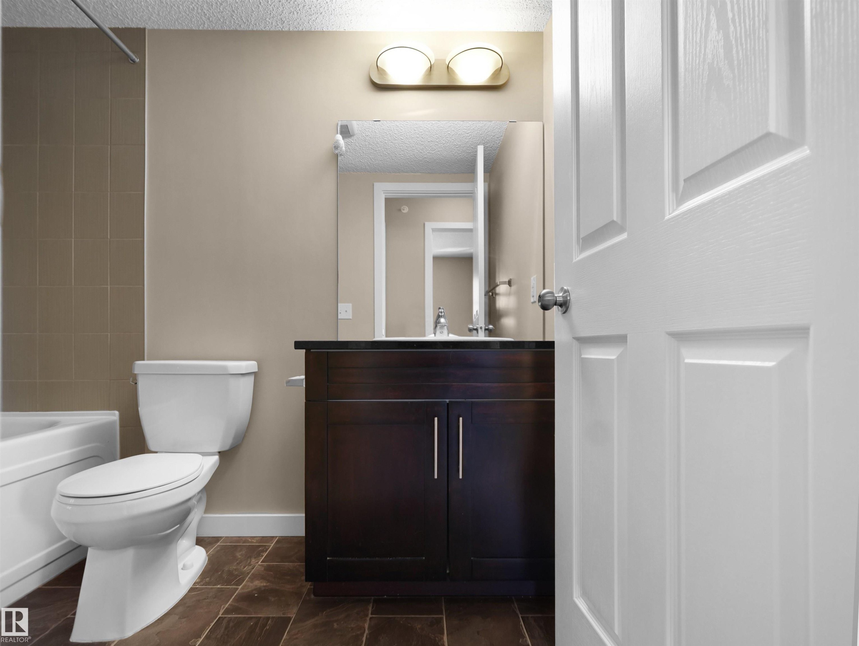 Bathroom featuring a dark wood-finish vanity with a dark countertop, an integrated sink, and a framed mirror - 417 1060 Mcconachie Boulevard, Edmonton, AB - Indoor Photo Showing Bathroom