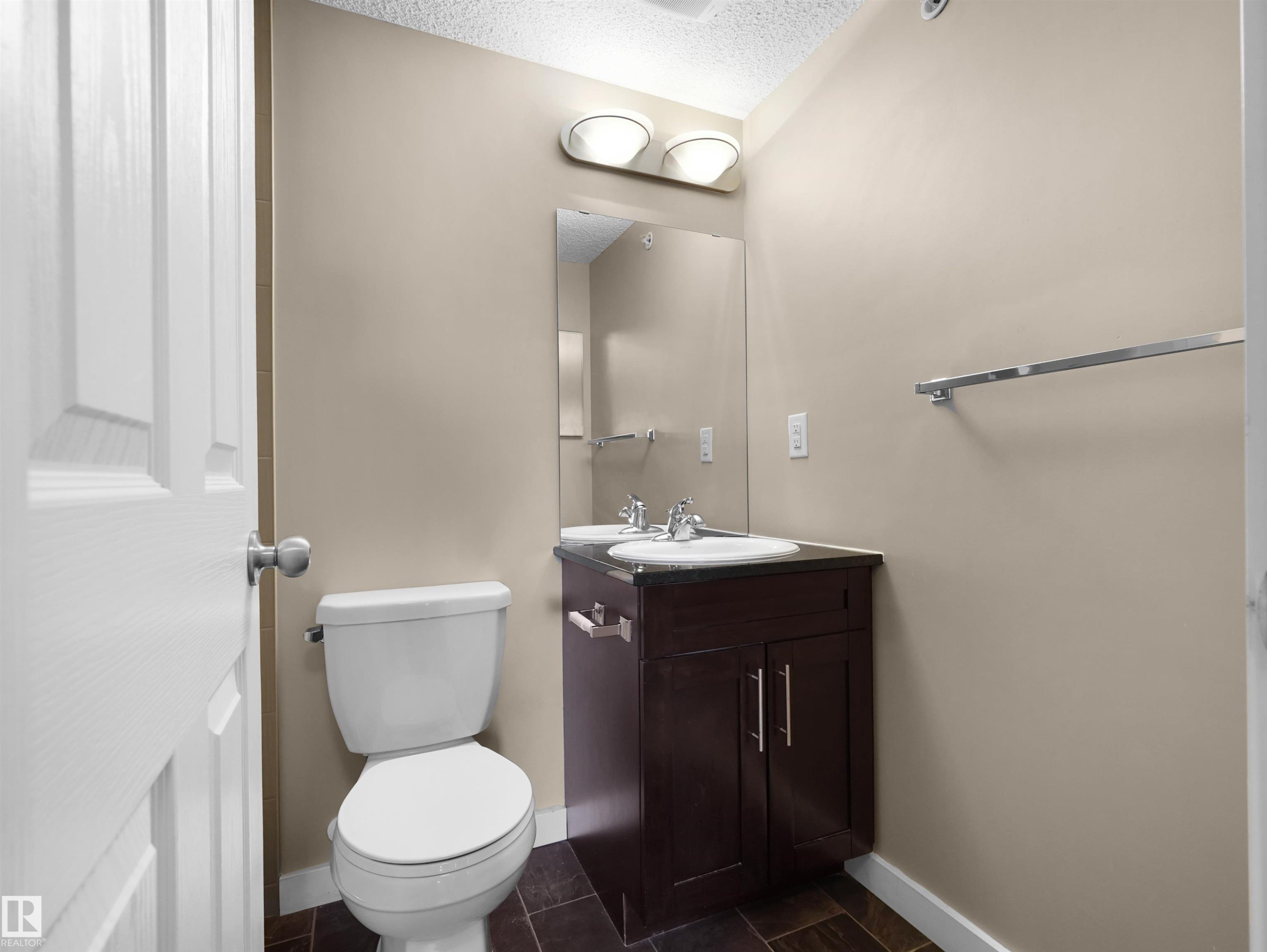 Bathroom featuring a dark wood-finish vanity with an integrated sink, polished chrome hardware, an overhead vanity light fixture, and tile flooring - 417 1060 Mcconachie Boulevard, Edmonton, AB - Indoor Photo Showing Bathroom