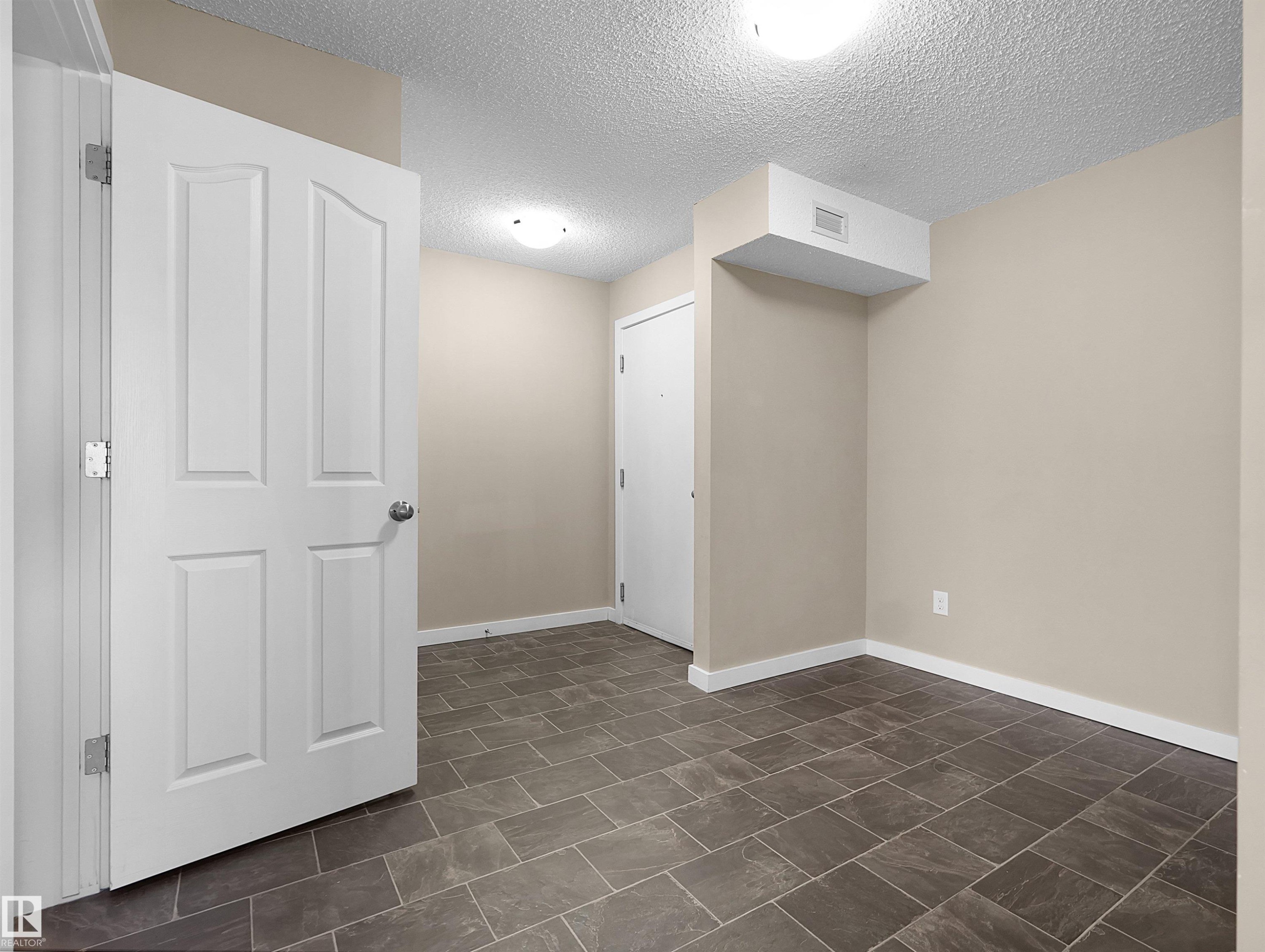 Rectangular tile flooring complements neutral-toned walls, contrasting with white trim and a white paneled door - 417 1060 Mcconachie Boulevard, Edmonton, AB - Indoor Photo Showing Other Room