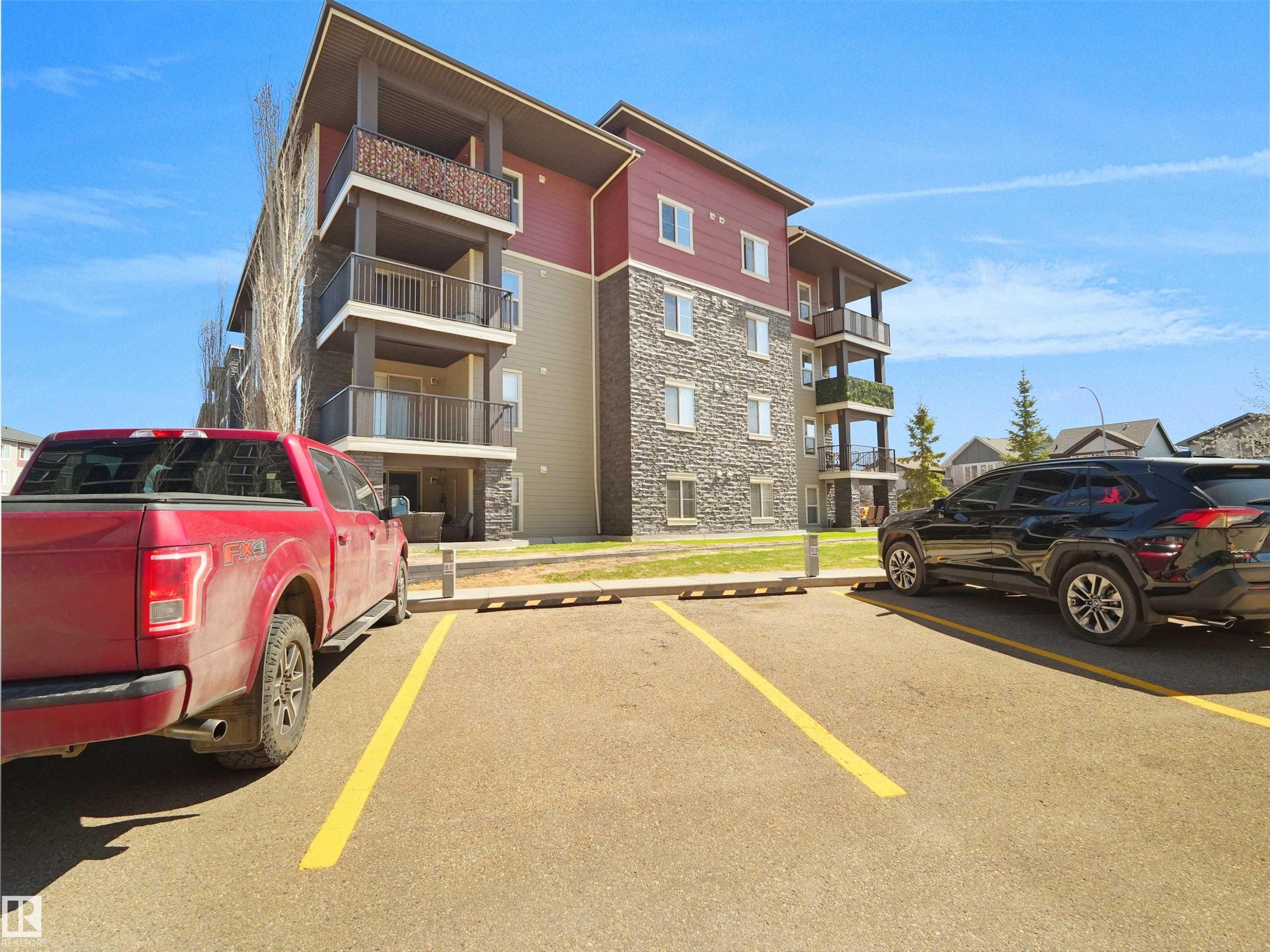 Exterior apartment building featuring stone and siding finishes, multiple private balconies with metal railings, and dedicated surface parking - 417 1060 Mcconachie Boulevard, Edmonton, AB - Outdoor With Balcony