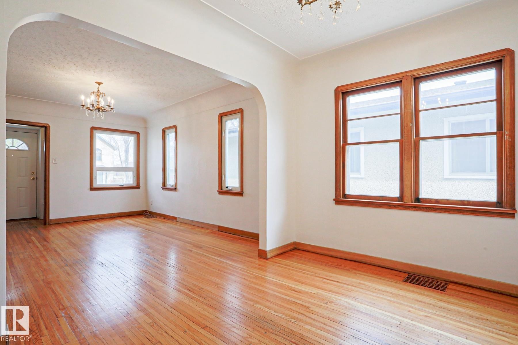 Spacious interior featuring wood-finish flooring throughout, an arched doorway, and multiple windows with warm wood trim - 9611 81 Avenue, Edmonton, AB - Indoor Photo Showing Other Room