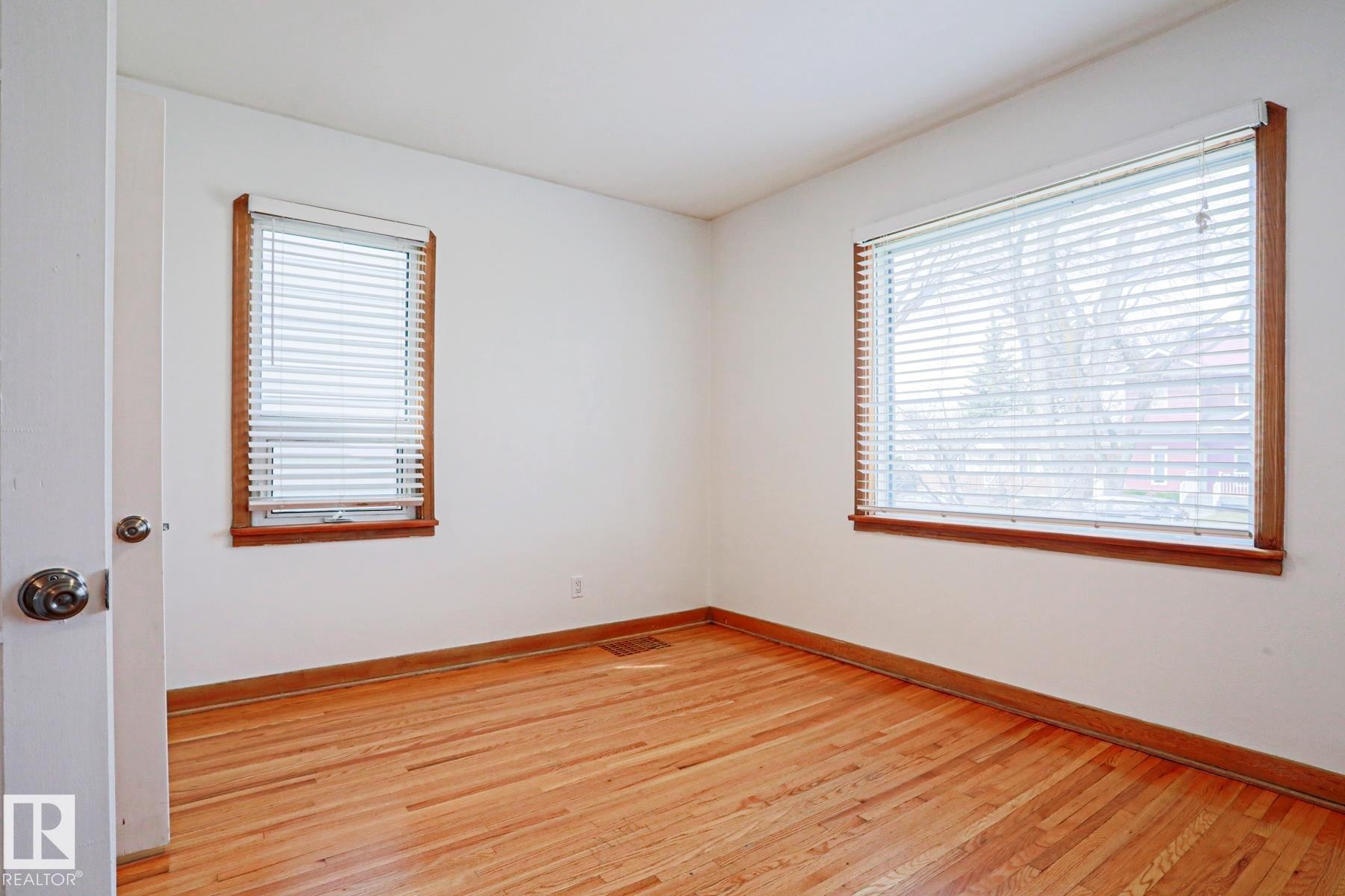 Hardwood flooring throughout featuring two windows with wood trim and horizontal blinds - 9611 81 Avenue, Edmonton, AB - Indoor Photo Showing Other Room