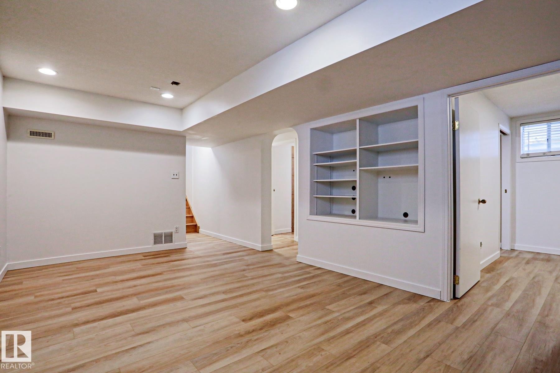 Spacious room featuring wood-finish flooring, recessed lighting, white walls, built-in shelving, and a visible window with blinds - 9611 81 Avenue, Edmonton, AB - Indoor Photo Showing Other Room