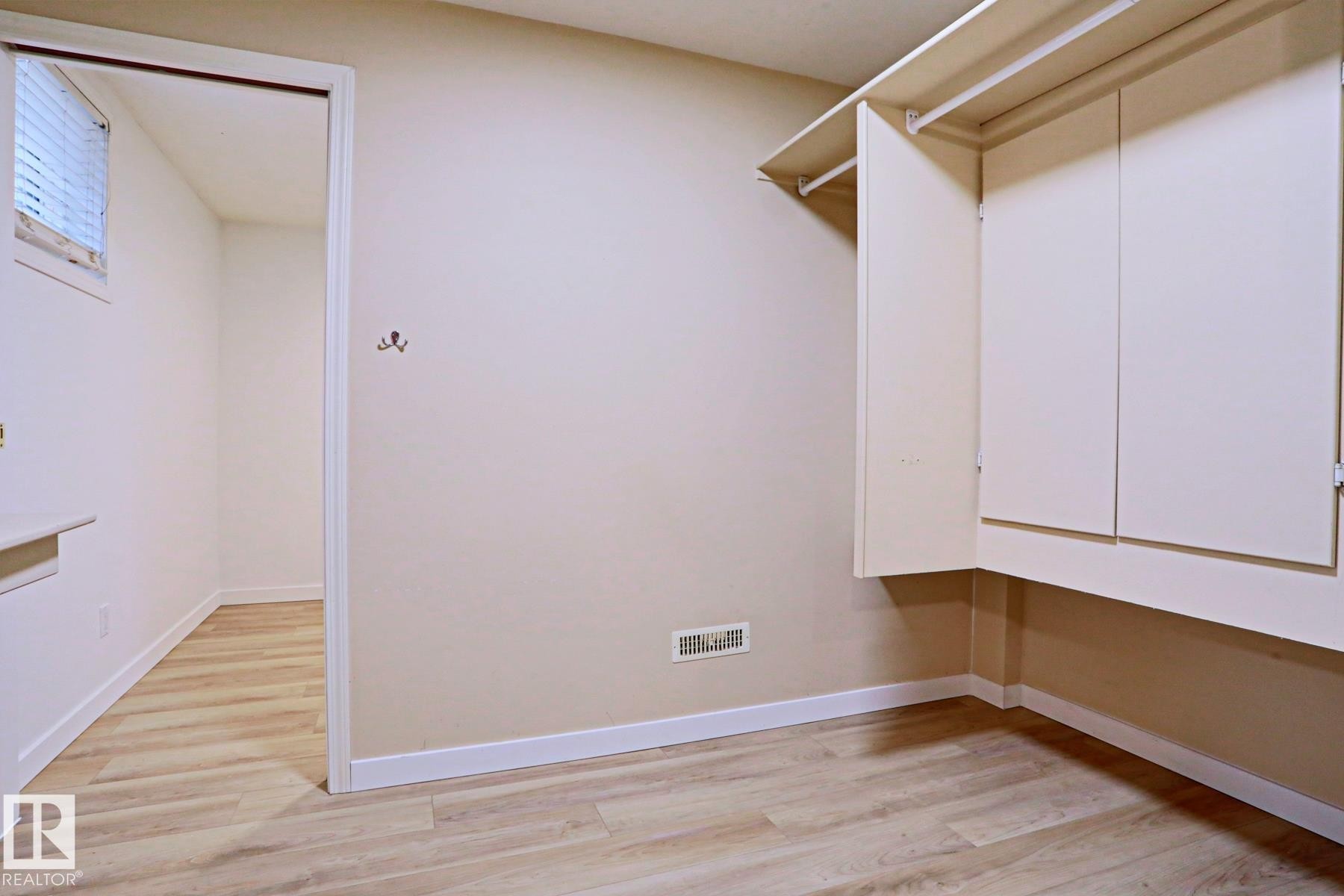 Room featuring light wood-finish flooring, white baseboards, a built-in closet with upper shelving and hanging rods, and a window with horizontal blinds - 9611 81 Avenue, Edmonton, AB - Indoor Photo Showing Other Room