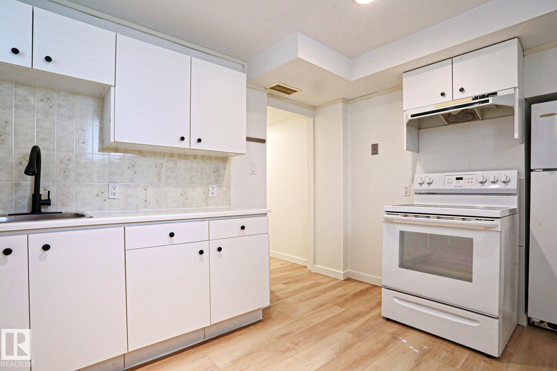 Kitchen featuring white cabinetry, light-toned wood-finish flooring, white countertops, a tile backsplash, and a matte black faucet - 9611 81 Avenue, Edmonton, AB - Indoor Photo Showing Kitchen