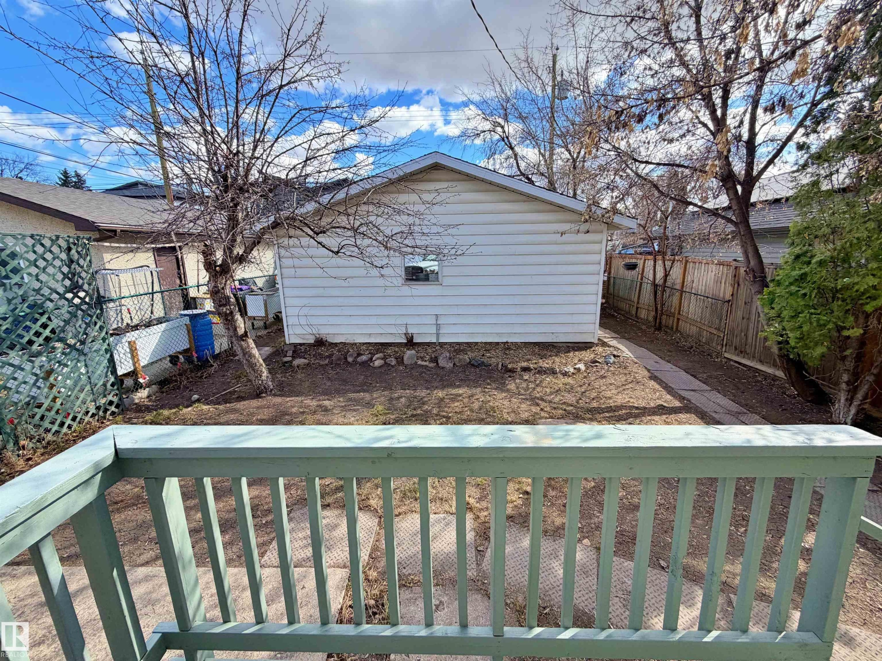 Expansive backyard featuring a detached garage with vinyl siding, natural wood fencing, a concrete paver pathway, and mature trees - 9611 81 Avenue, Edmonton, AB - Outdoor