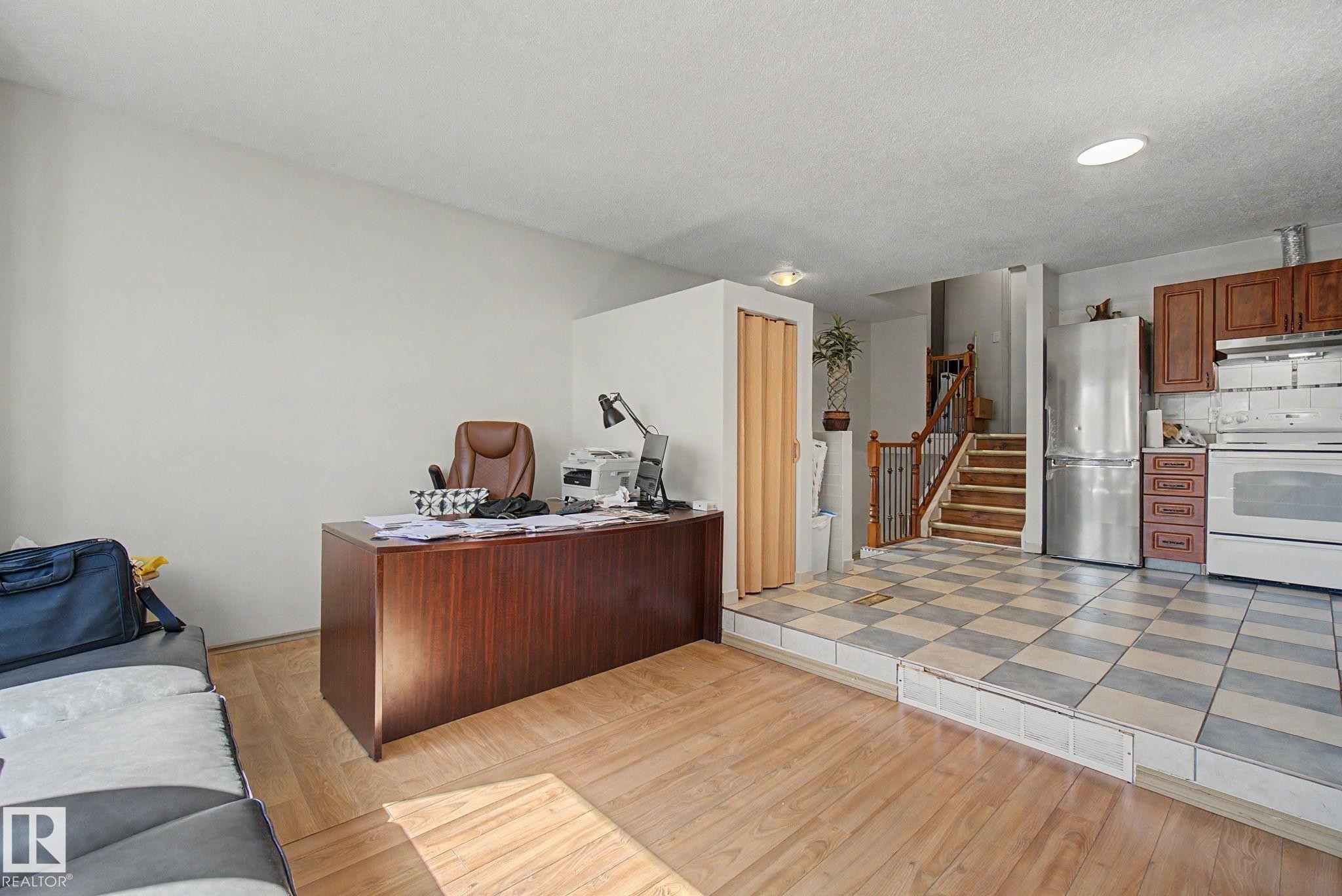Open-concept living space featuring wood-finish flooring, a raised kitchen area with checkered tile, wood cabinetry, and stainless steel appliances - 4106 38 Street, Edmonton, AB - Indoor