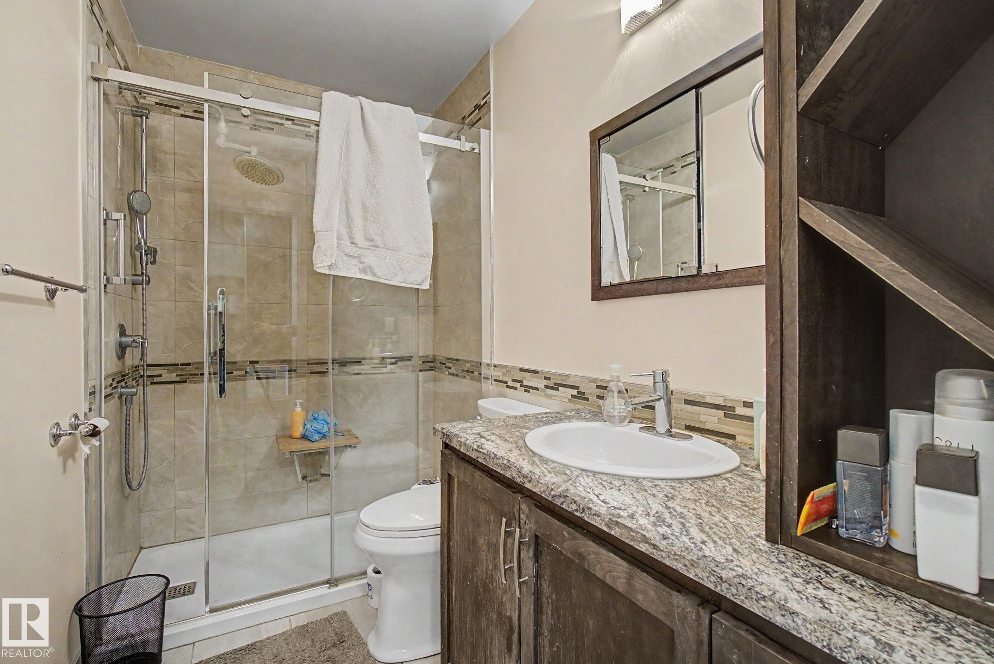 Bathroom featuring a glass-enclosed shower with tile surround, a built-in shower bench, and a rain showerhead - 4106 38 Street, Edmonton, AB - Indoor Photo Showing Bathroom