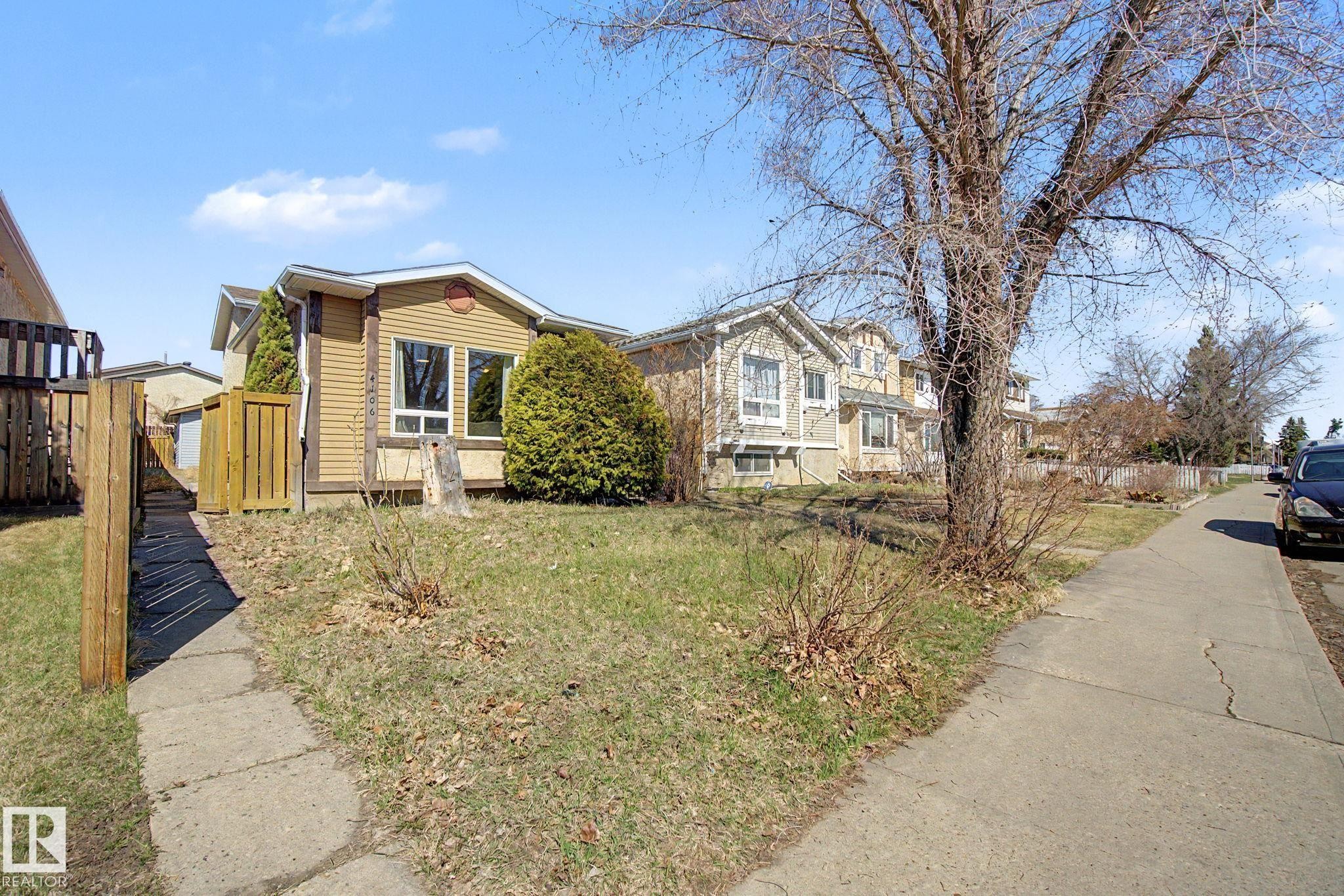 Exterior property featuring tan siding, a concrete pathway, a wooden fence, and established landscaping - 4106 38 Street, Edmonton, AB - Outdoor