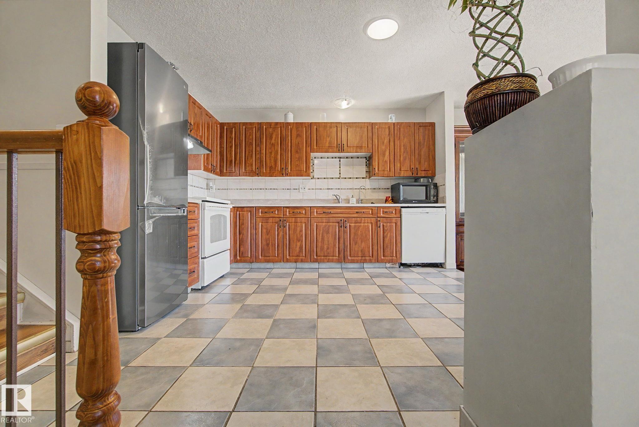 Kitchen featuring wood cabinetry, stainless steel refrigerator, white range, white dishwasher, and checkerboard floor tiles - 4106 38 Street, Edmonton, AB - Indoor Photo Showing Kitchen