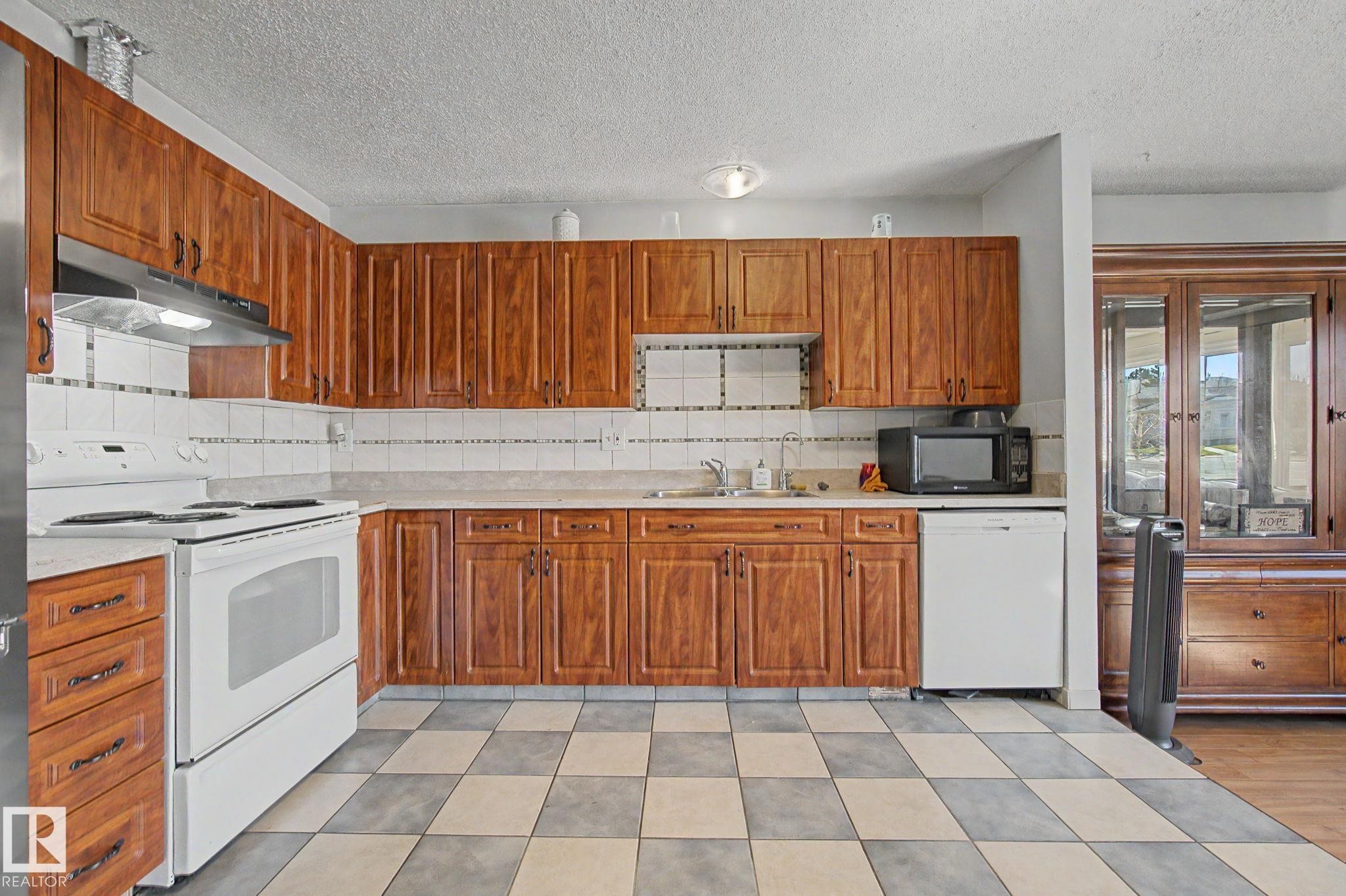 Kitchen featuring ample wood cabinetry, a white tile backsplash, and a checkerboard floor pattern - 4106 38 Street, Edmonton, AB - Indoor Photo Showing Kitchen With Double Sink