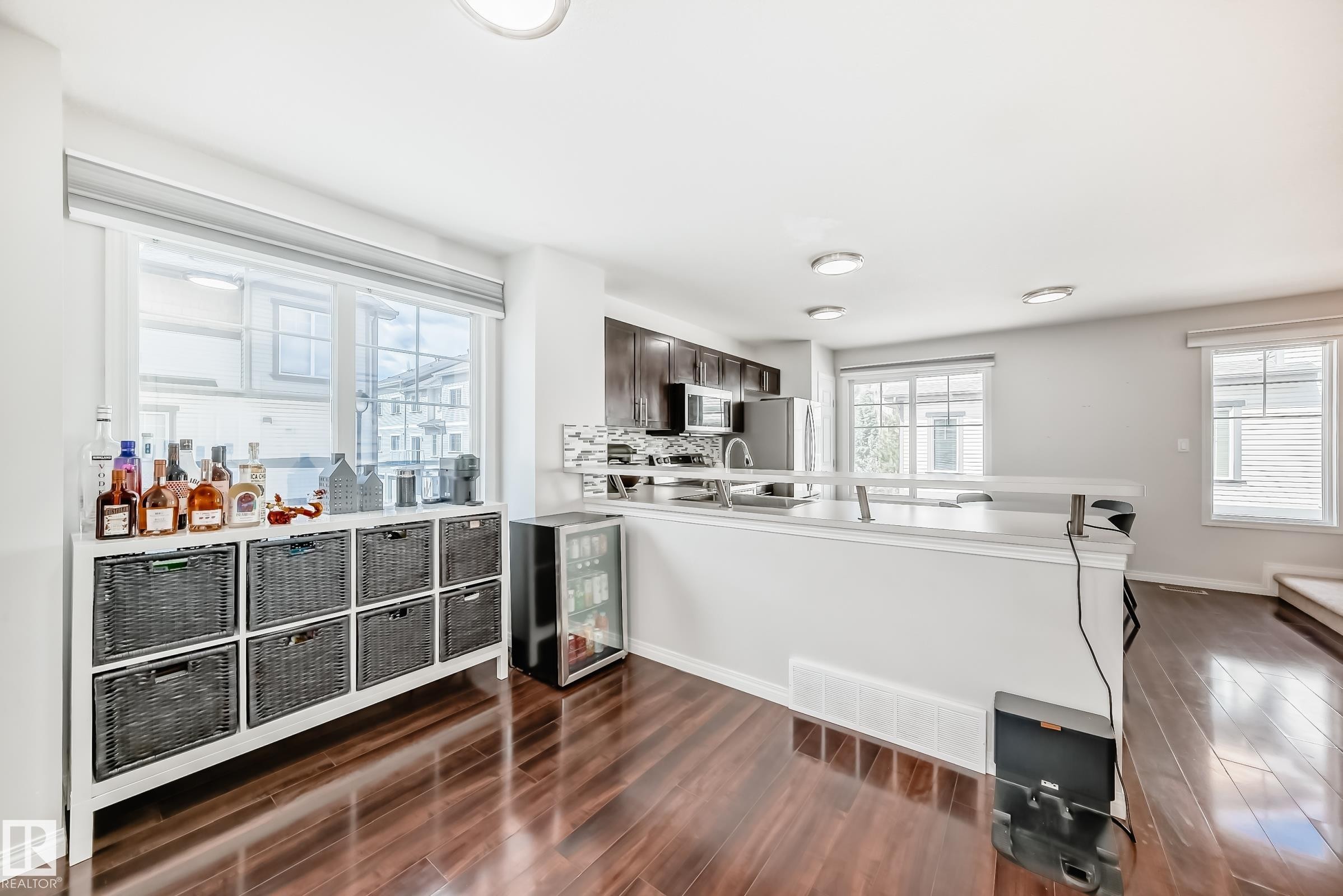 Open-concept living space with dark wood-finish flooring, recessed ceiling lighting, and a kitchen featuring dark cabinetry, stainless steel appliances, and a light-toned countertop - 45 4850 Terwillegar Common, Edmonton, AB - Indoor Photo Showing Other Room
