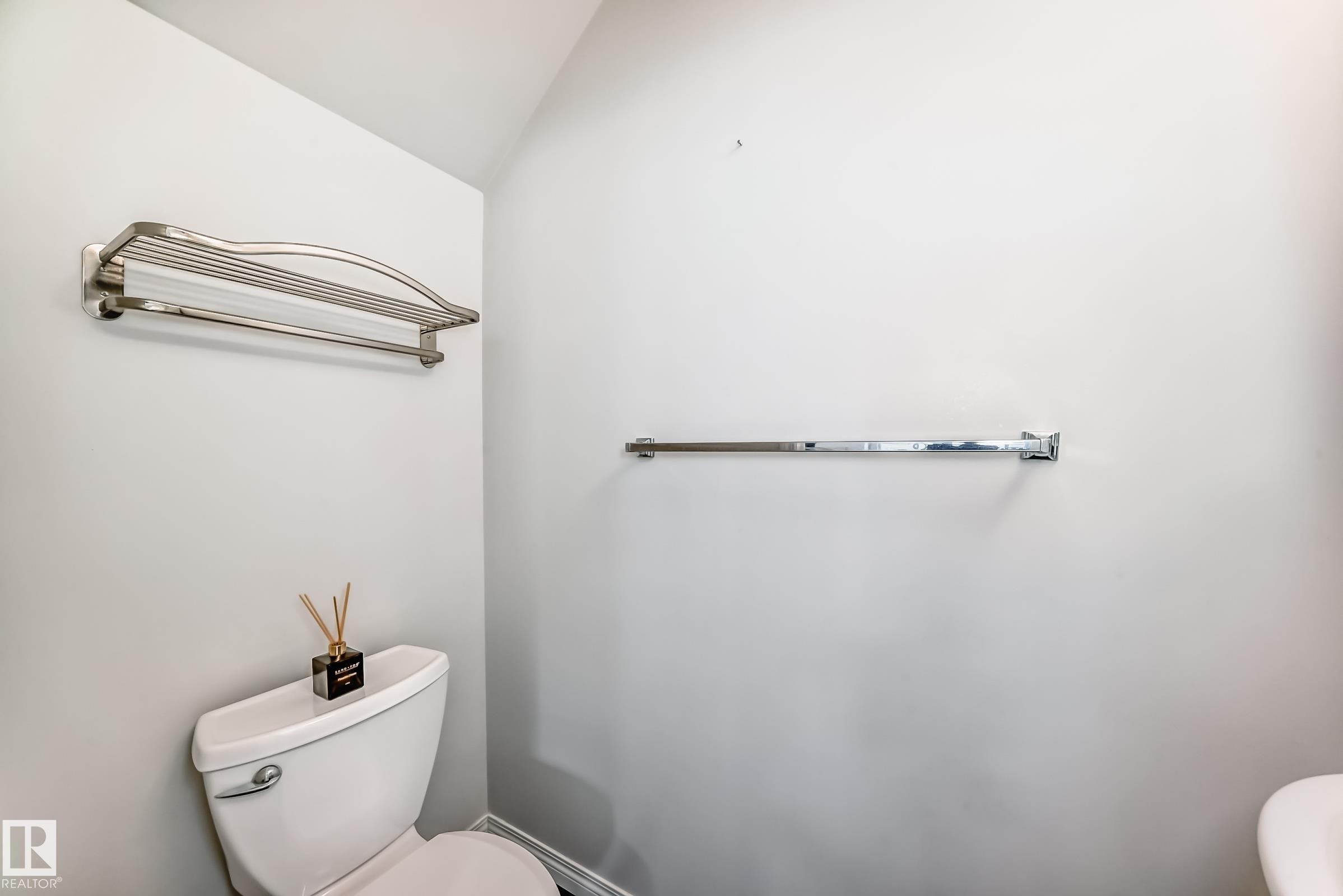 White toilet with a chrome flush lever, a wall-mounted chrome towel bar, and a brushed nickel towel shelf - 45 4850 Terwillegar Common, Edmonton, AB - Indoor Photo Showing Bathroom