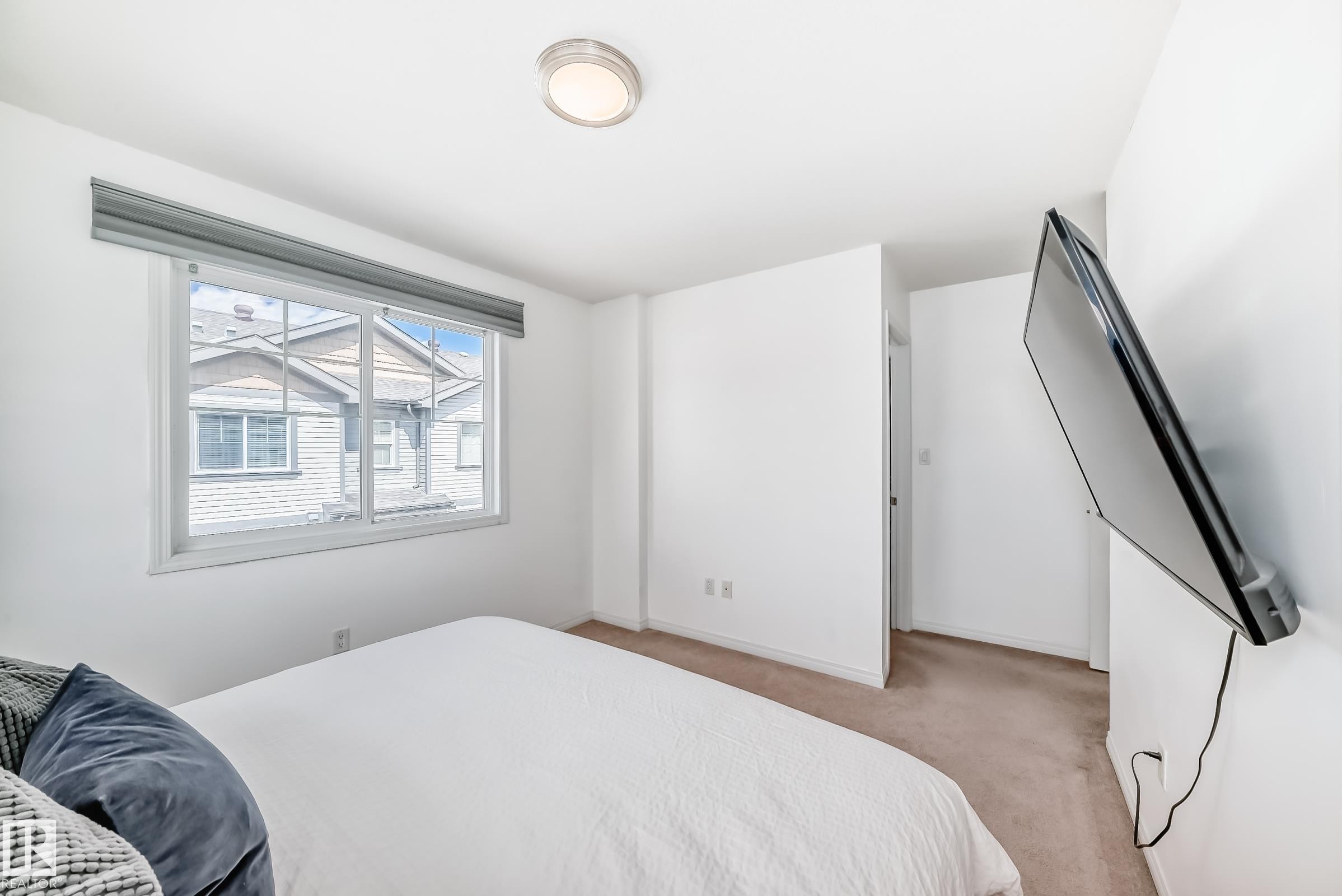 Carpeted room with white walls, a large window with a gray roller shade, and a flush mount ceiling light - 45 4850 Terwillegar Common, Edmonton, AB - Indoor Photo Showing Bedroom