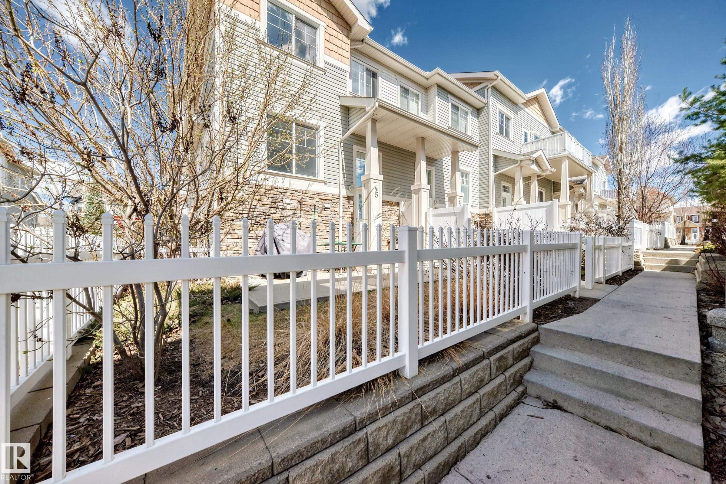 Townhome exterior featuring horizontal siding, stone veneer accents, and white picket fencing - 45 4850 Terwillegar Common, Edmonton, AB - Outdoor With Deck Patio Veranda