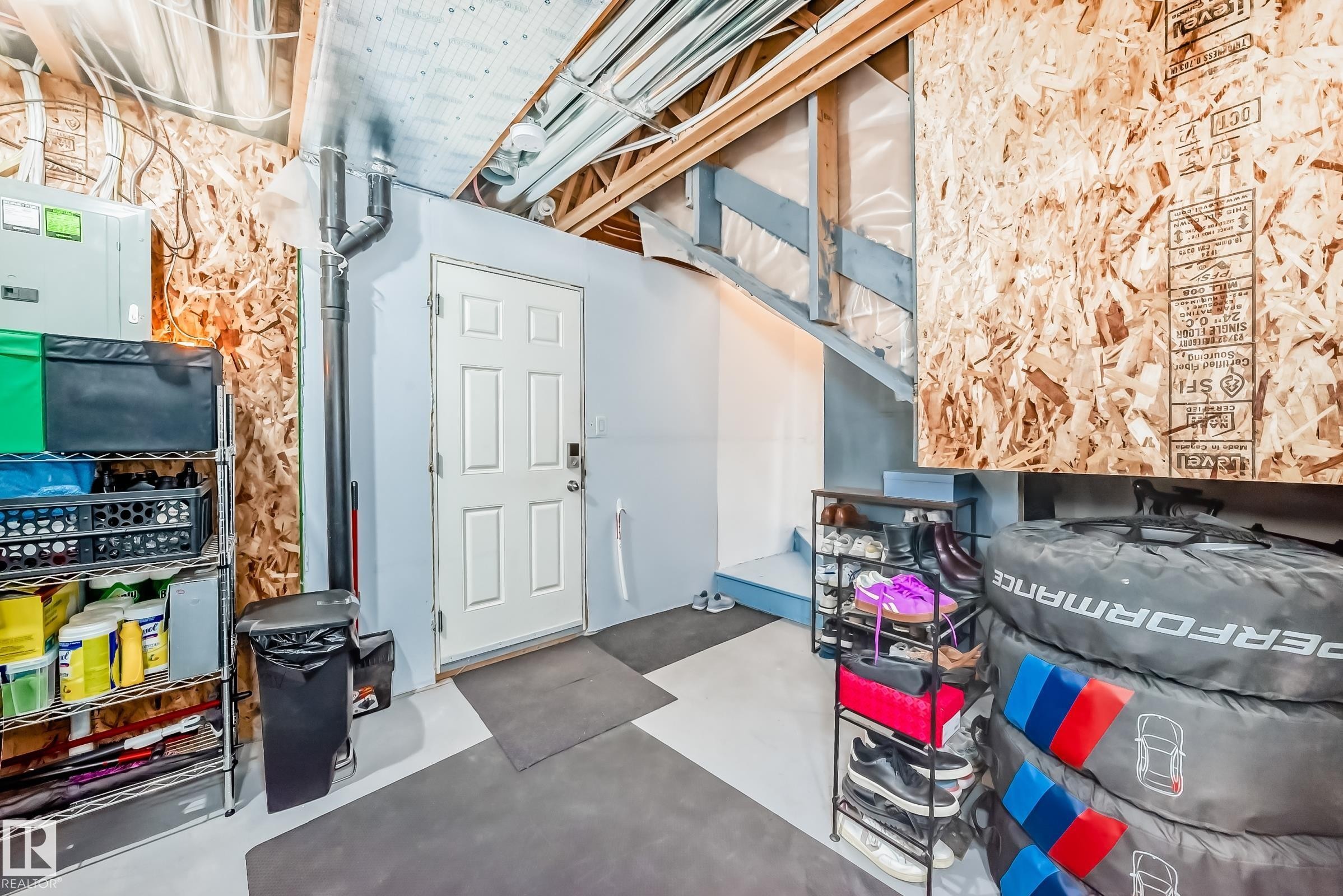 Basement area featuring a painted concrete floor, exposed ceiling joists, a finished stairway with wood railings, and a six-panel door - 45 4850 Terwillegar Common, Edmonton, AB -