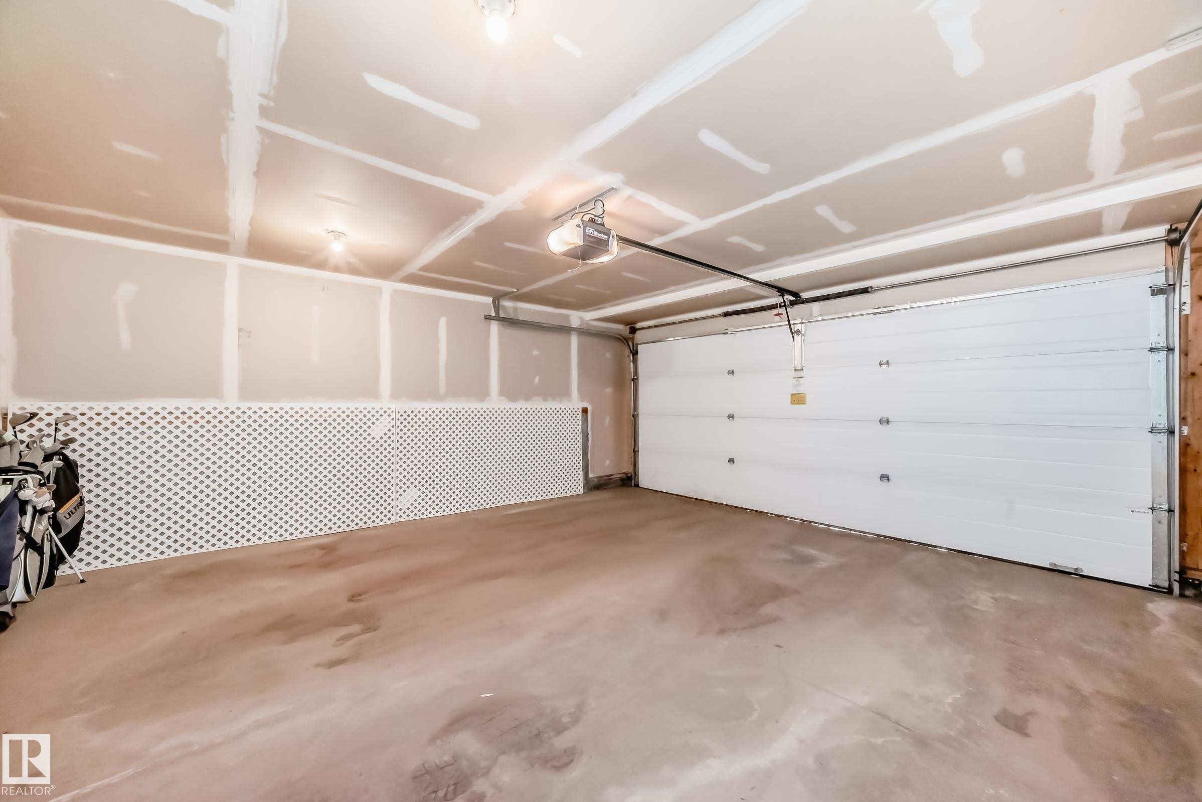 Spacious garage featuring a concrete floor, an overhead garage door opener, and unfinished drywall walls - 45 4850 Terwillegar Common, Edmonton, AB - Indoor Photo Showing Garage