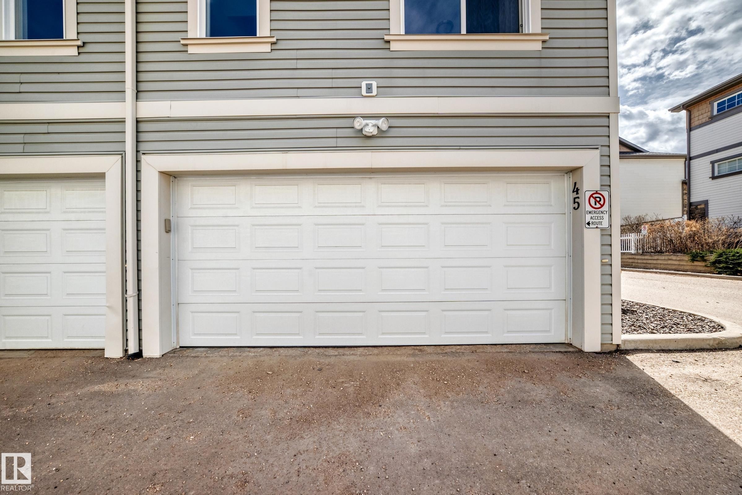 Exterior featuring horizontal siding, white panel garage door, and light fixture - 45 4850 Terwillegar Common, Edmonton, AB - Outdoor With Exterior