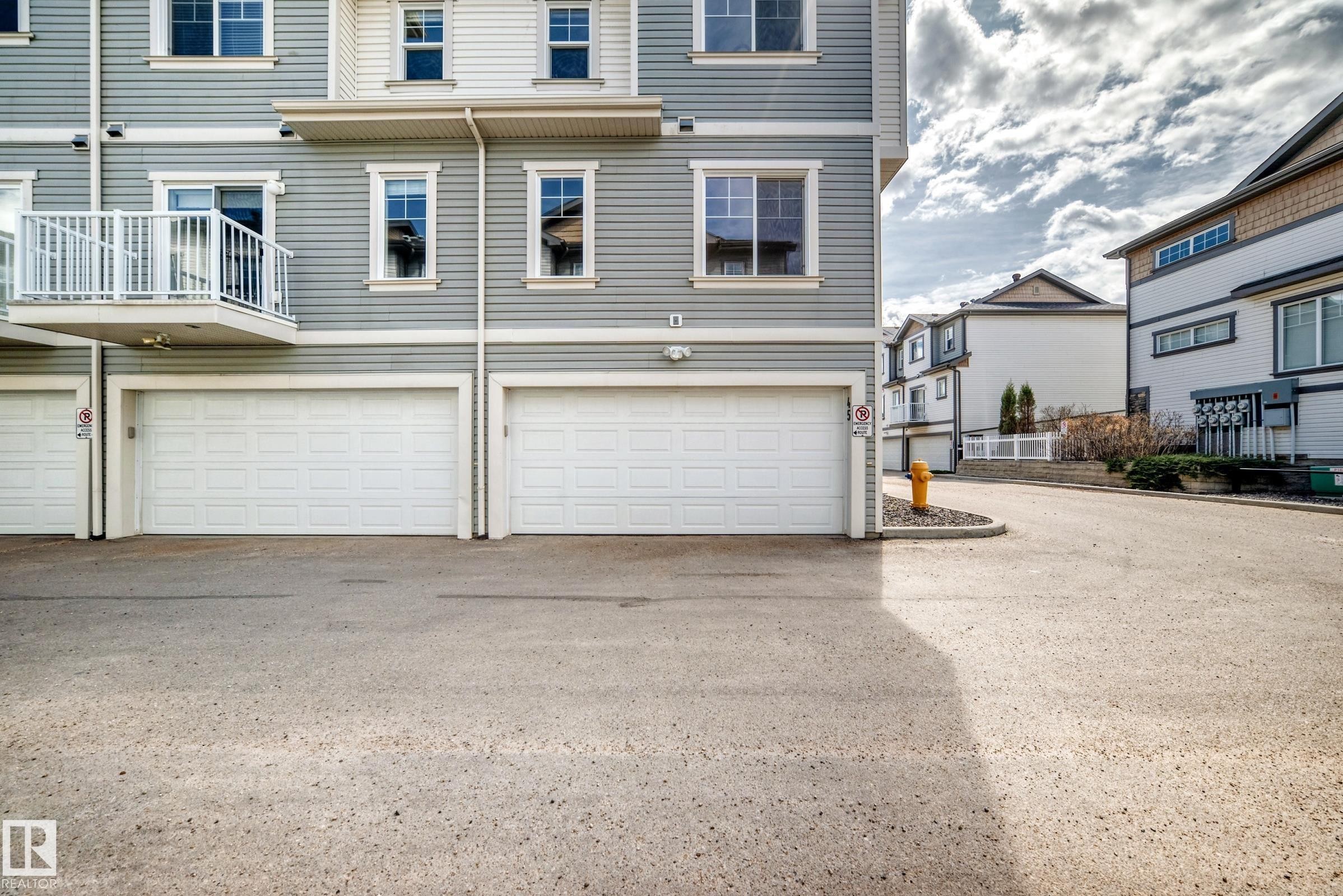 Grey vinyl siding exterior with white trim, featuring three integrated garage doors, a private balcony with white railings, and multiple windows - 45 4850 Terwillegar Common, Edmonton, AB - Outdoor