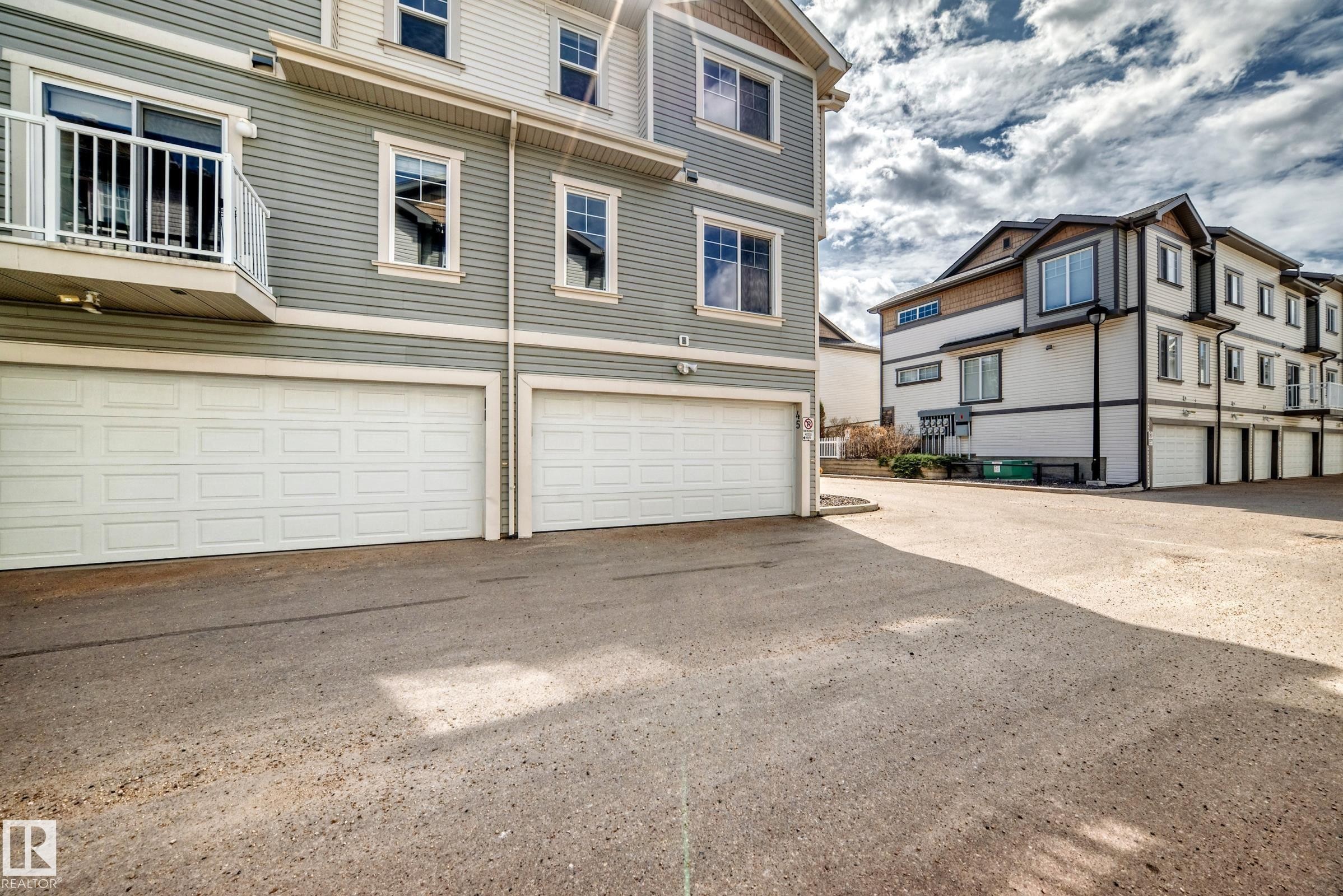 Exterior featuring two garages with white panel doors, light grey siding, and white trim windows - 45 4850 Terwillegar Common, Edmonton, AB - Outdoor
