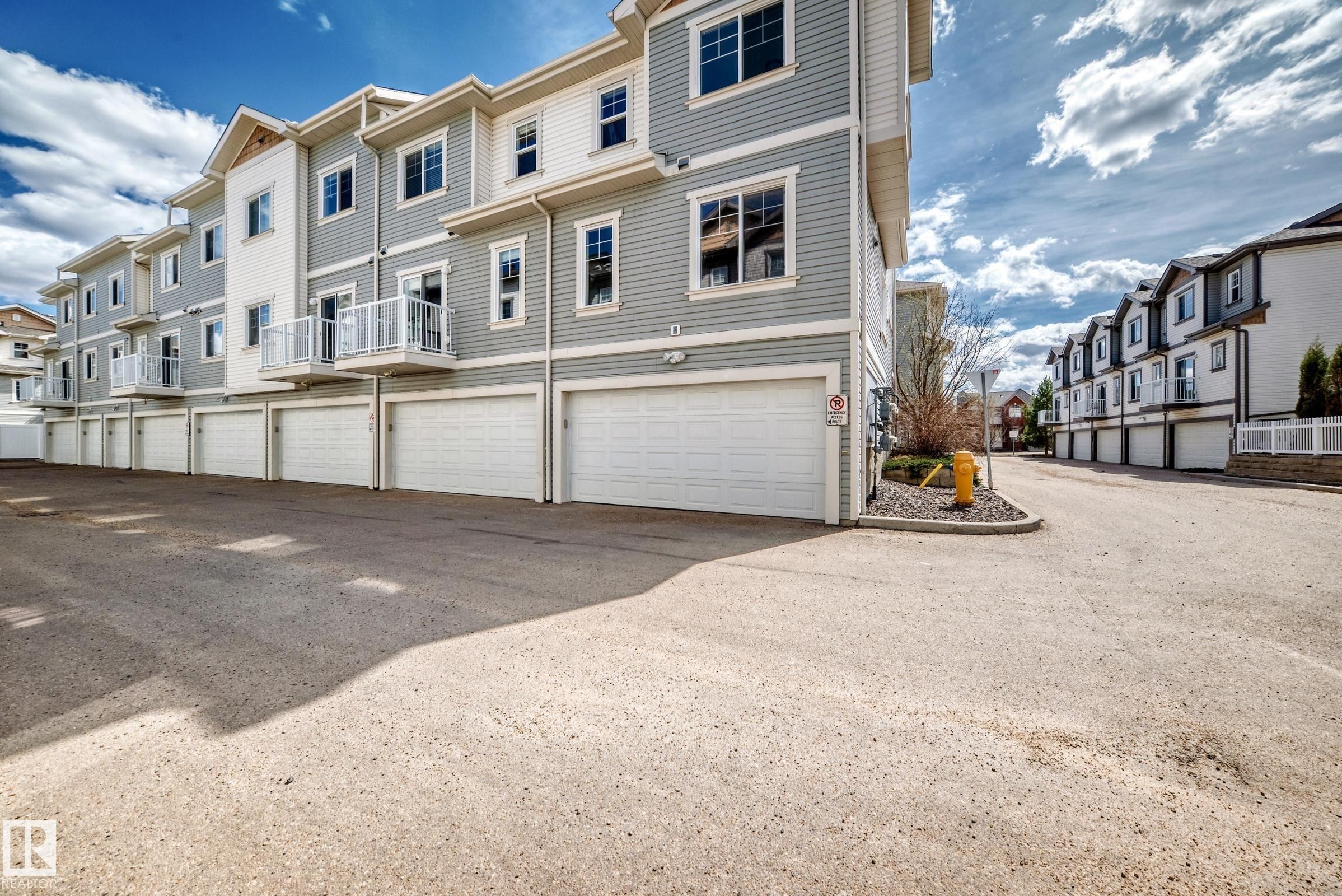 Townhome exterior featuring light gray siding with white trim, multiple attached garages, and private balconies with white railings - 45 4850 Terwillegar Common, Edmonton, AB - Outdoor