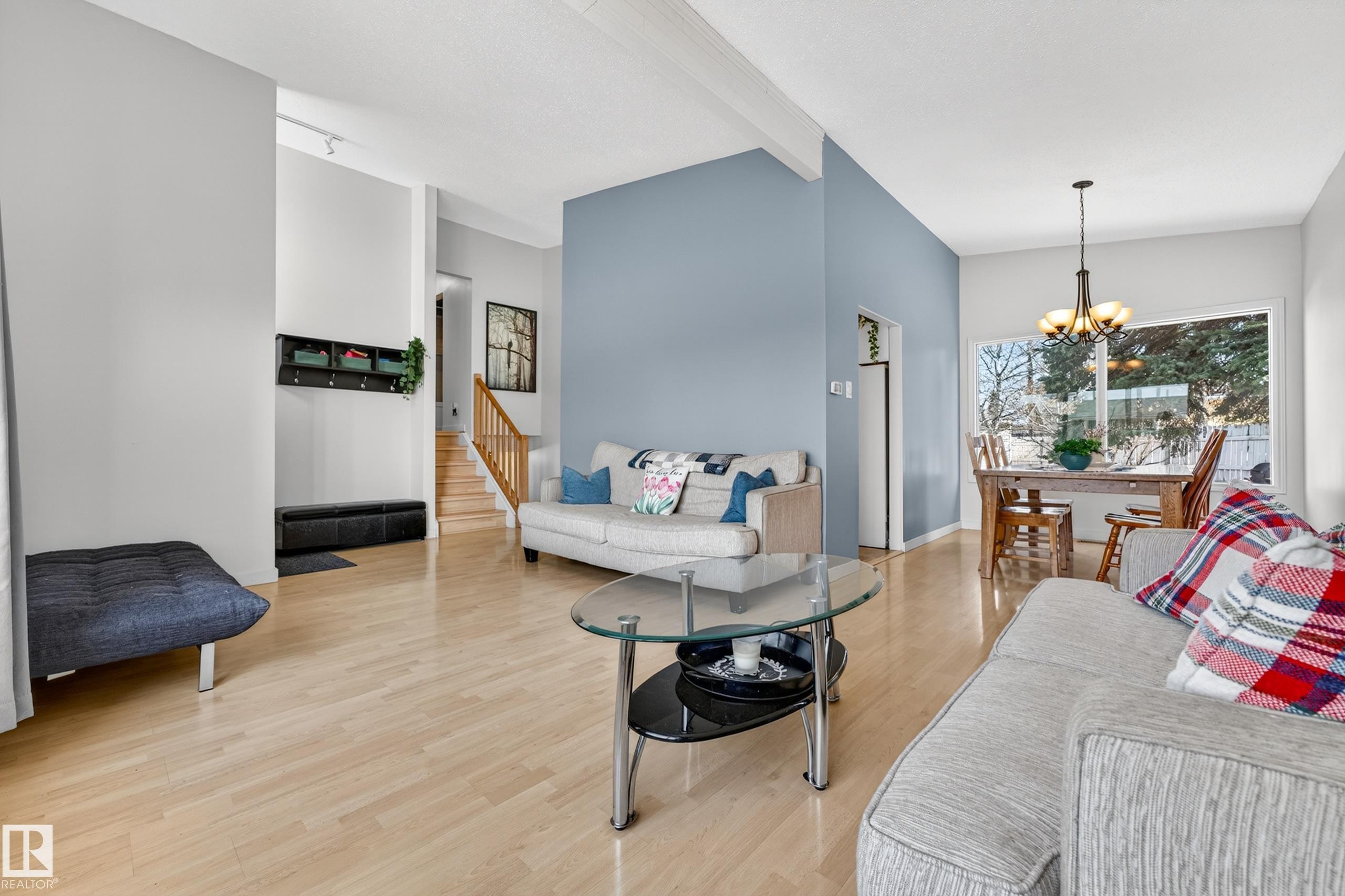 Open-concept living area with light wood-finish flooring, vaulted ceilings with exposed beams, and a prominent blue accent wall - 5304 90A Avenue, Edmonton, AB - Indoor Photo Showing Other Room
