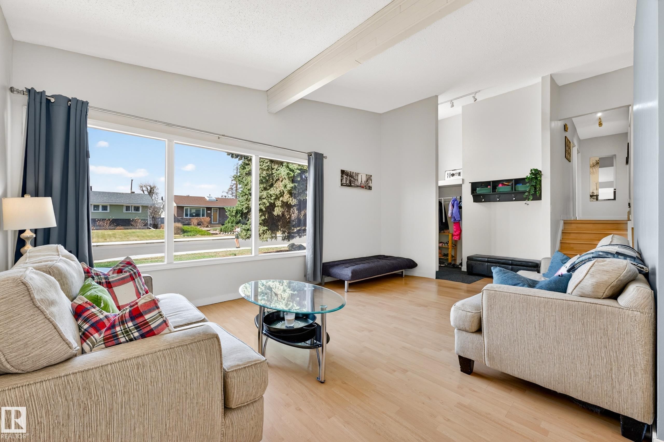Bright living area featuring expansive windows, wood-finish flooring, vaulted ceilings with exposed beams, and a built-in entry coat closet - 5304 90A Avenue, Edmonton, AB - Indoor Photo Showing Living Room