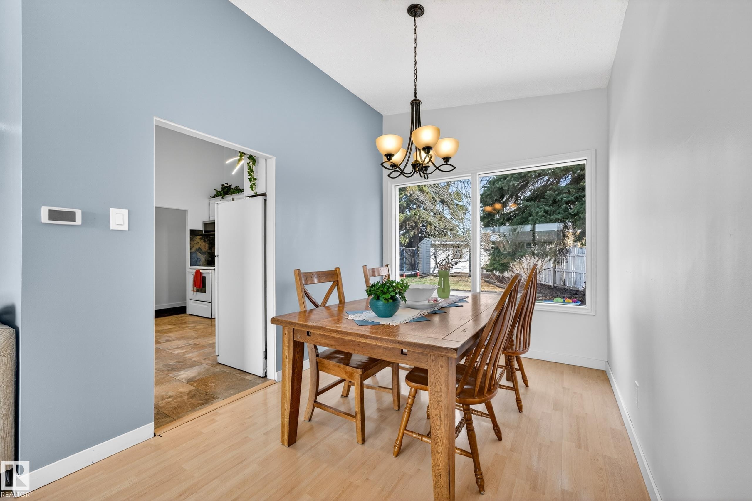 Dining area featuring wood-finish flooring, a contemporary chandelier, and a large window overlooking the backyard - 5304 90A Avenue, Edmonton, AB - Indoor Photo Showing Dining Room