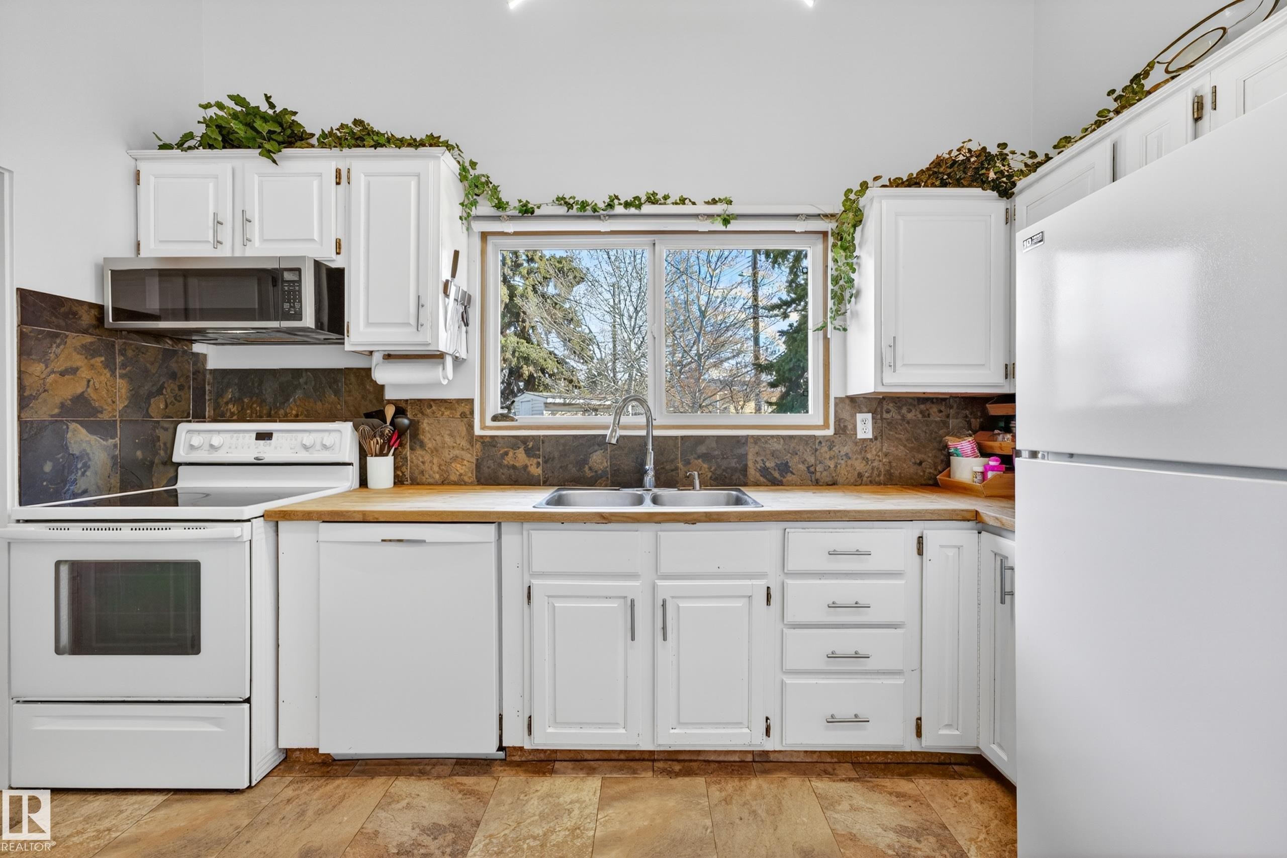 Kitchen featuring white cabinetry, light wood-finish countertops, and a dark stone tile backsplash - 5304 90A Avenue, Edmonton, AB - Indoor Photo Showing Kitchen With Double Sink