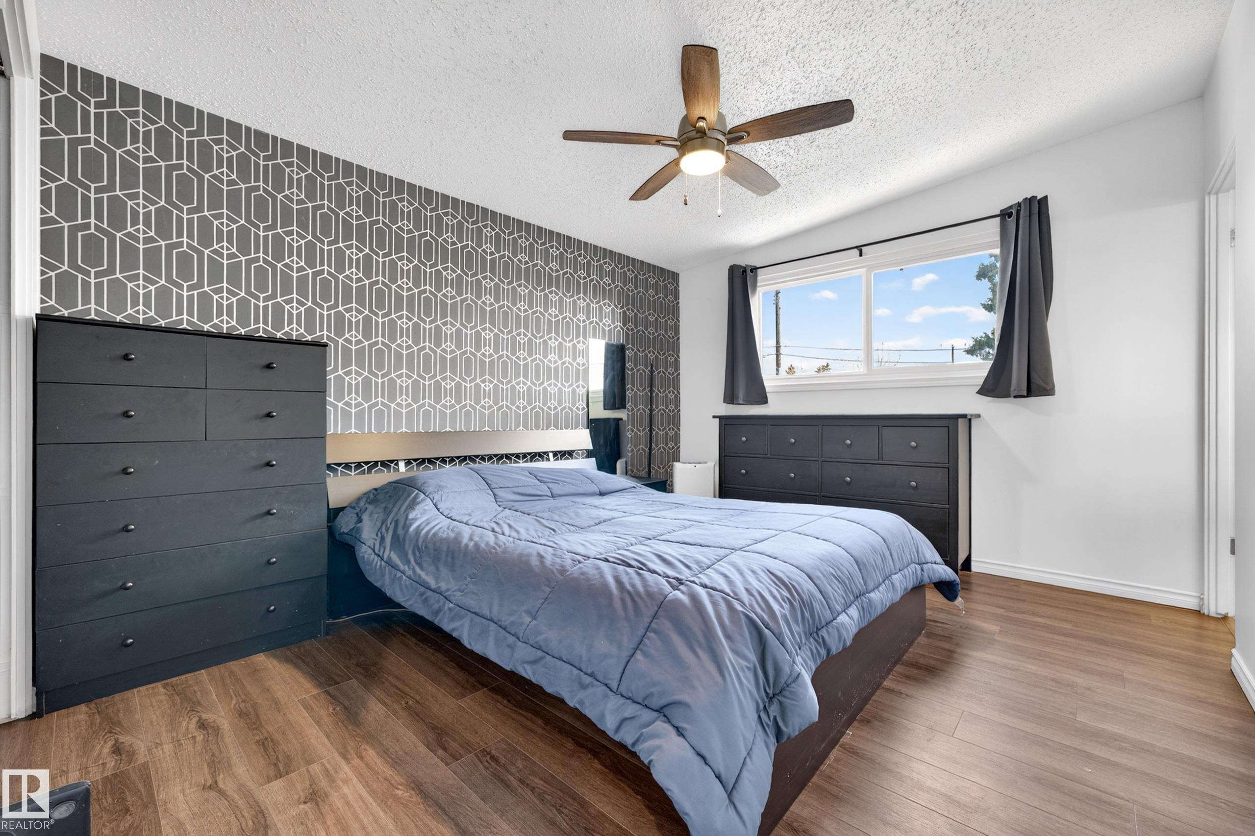 Bedroom featuring wood-finish flooring, a geometric accent wall, and a ceiling fan - 5304 90A Avenue, Edmonton, AB - Indoor Photo Showing Bedroom
