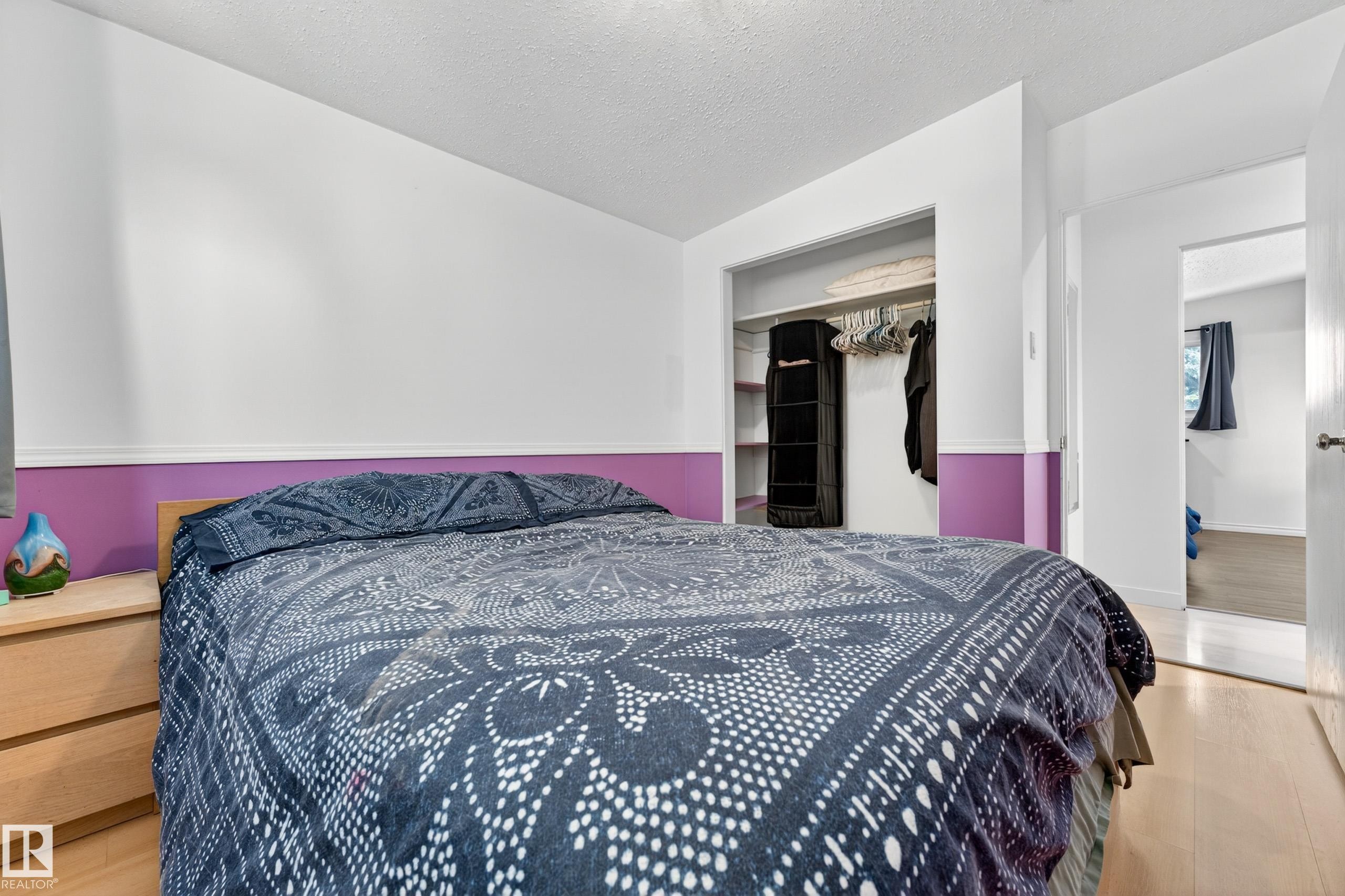 Bedroom featuring light wood-finish flooring, white walls with a purple accent band, and an open closet with shelving and hanging space - 5304 90A Avenue, Edmonton, AB - Indoor Photo Showing Bedroom