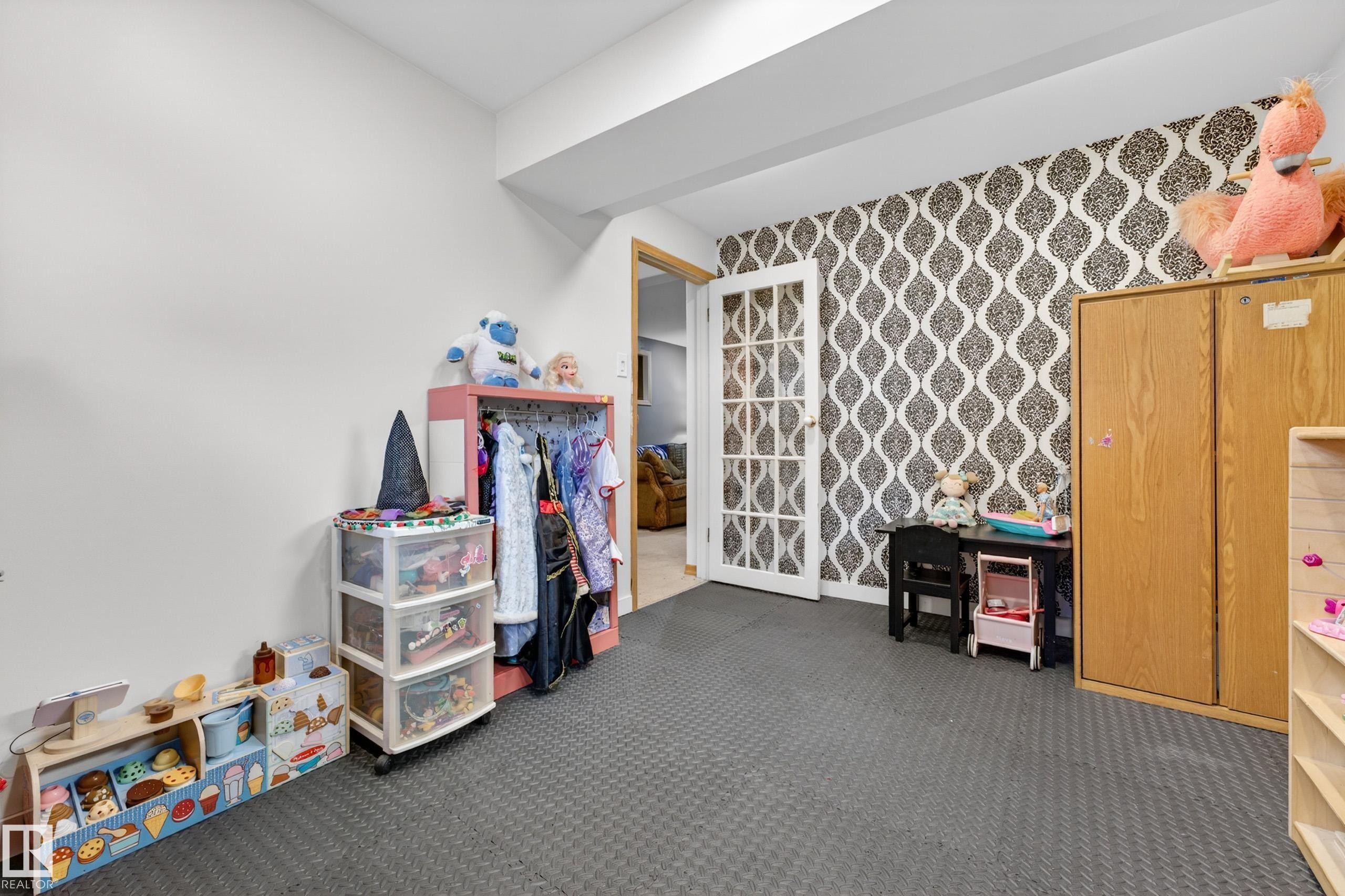 Flexible-use room featuring a patterned accent wall, white French doors, and durable interlocking foam tile flooring - 5304 90A Avenue, Edmonton, AB - Indoor
