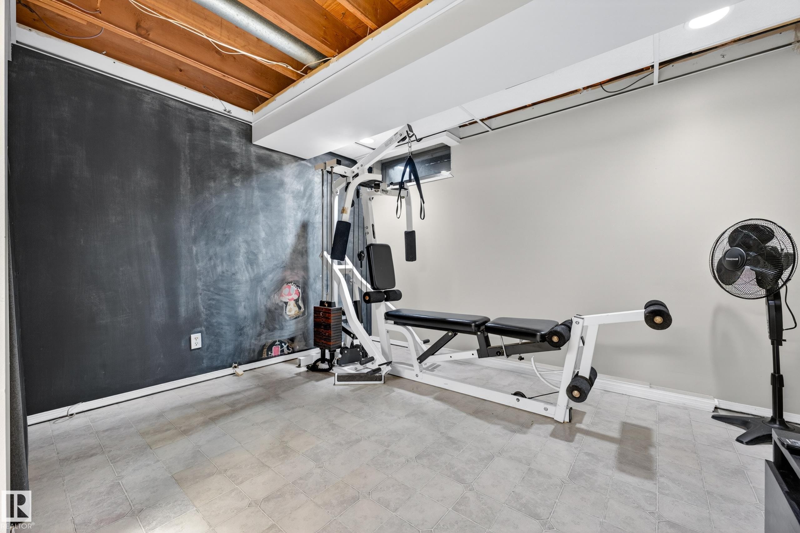 Finished basement space featuring light gray tile flooring, a dark accent wall, a light-colored wall, an exposed wood beam ceiling, and a small window - 5304 90A Avenue, Edmonton, AB - Indoor Photo Showing Gym Room