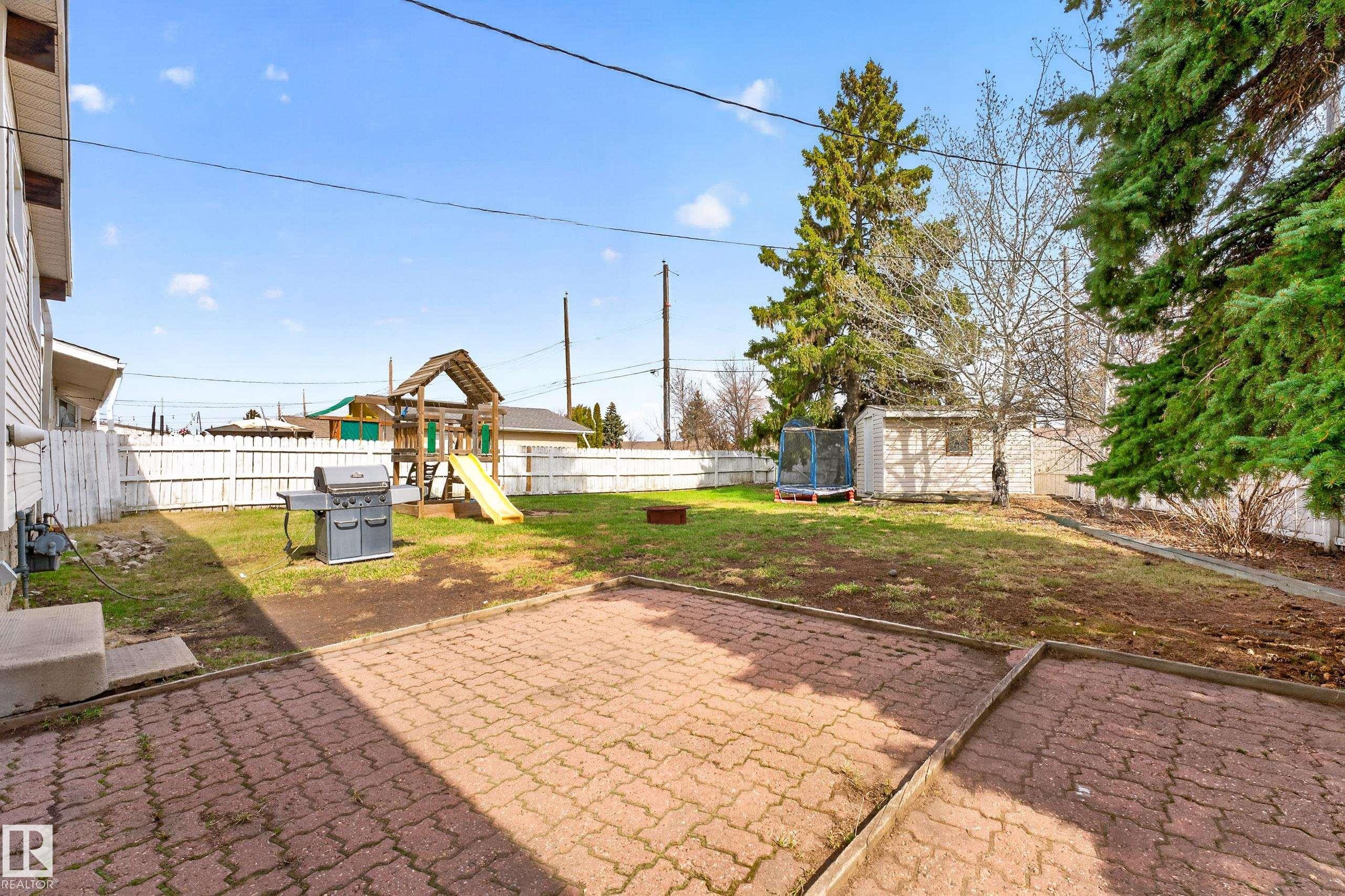 Expansive backyard featuring a red paver patio, a white picket fence, and mature evergreen trees - 5304 90A Avenue, Edmonton, AB - Outdoor