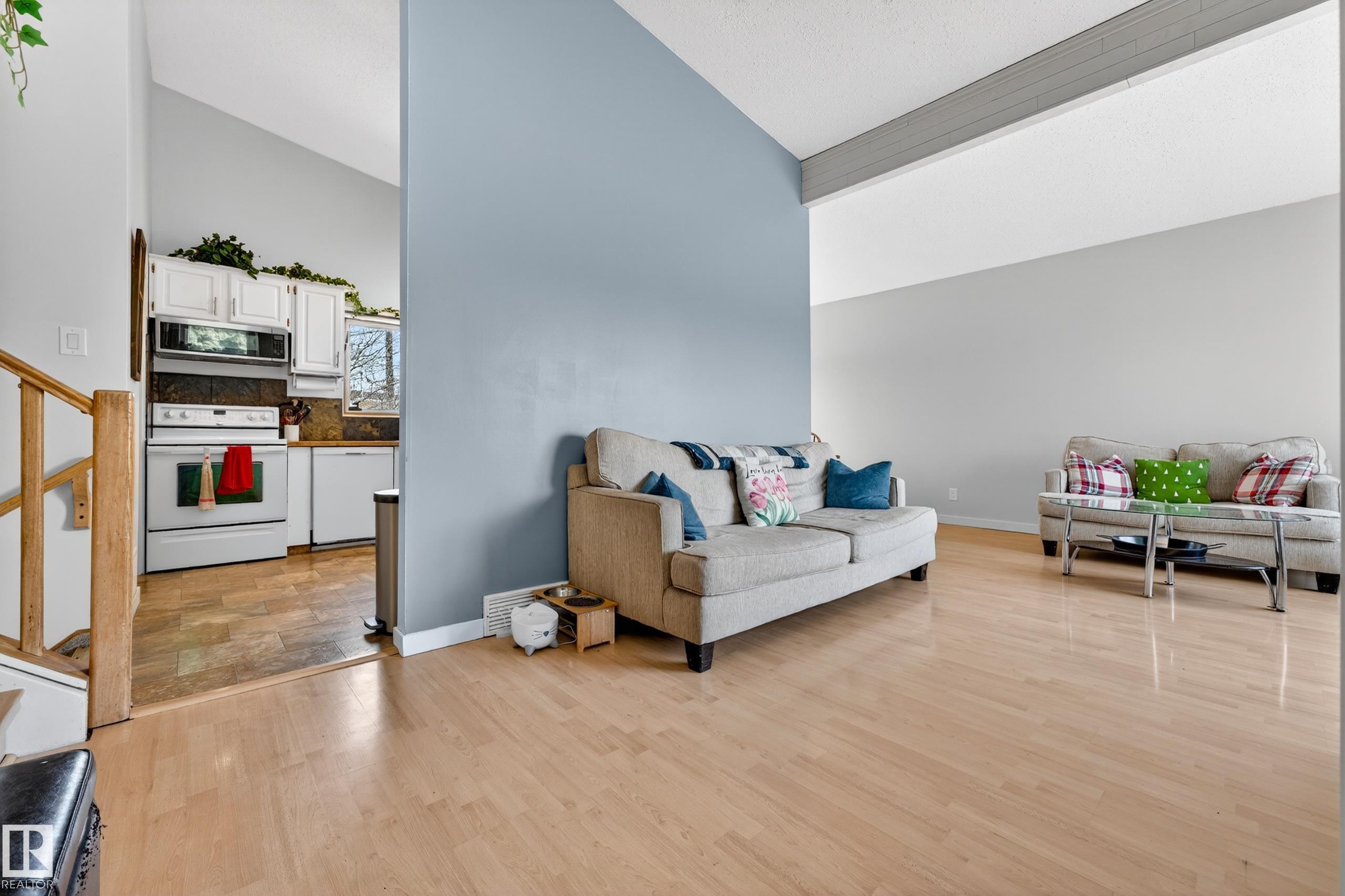 Bright living area featuring light wood-finish flooring, a vaulted ceiling, and a prominent blue accent wall - 5304 90A Avenue, Edmonton, AB - Indoor