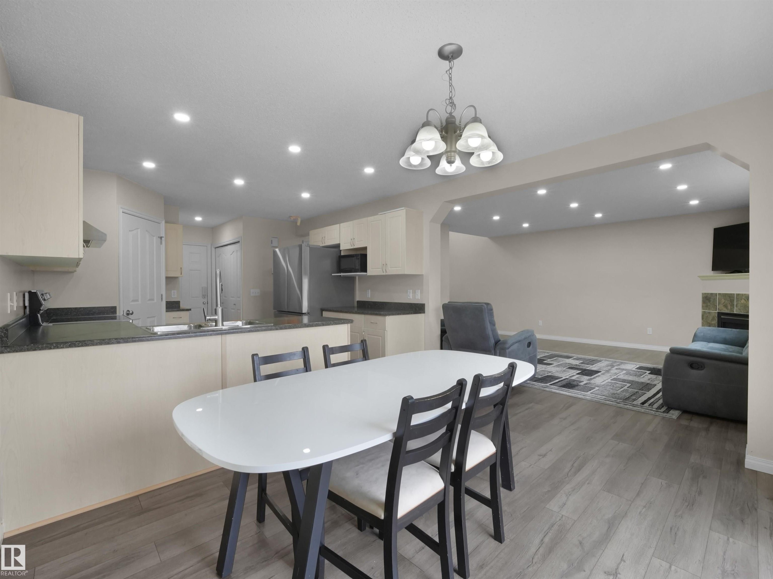 Open-concept kitchen and living area featuring wood-finish flooring, recessed lighting, and a fireplace with tile surround - 7407 Singer Landing, Edmonton, AB - Indoor