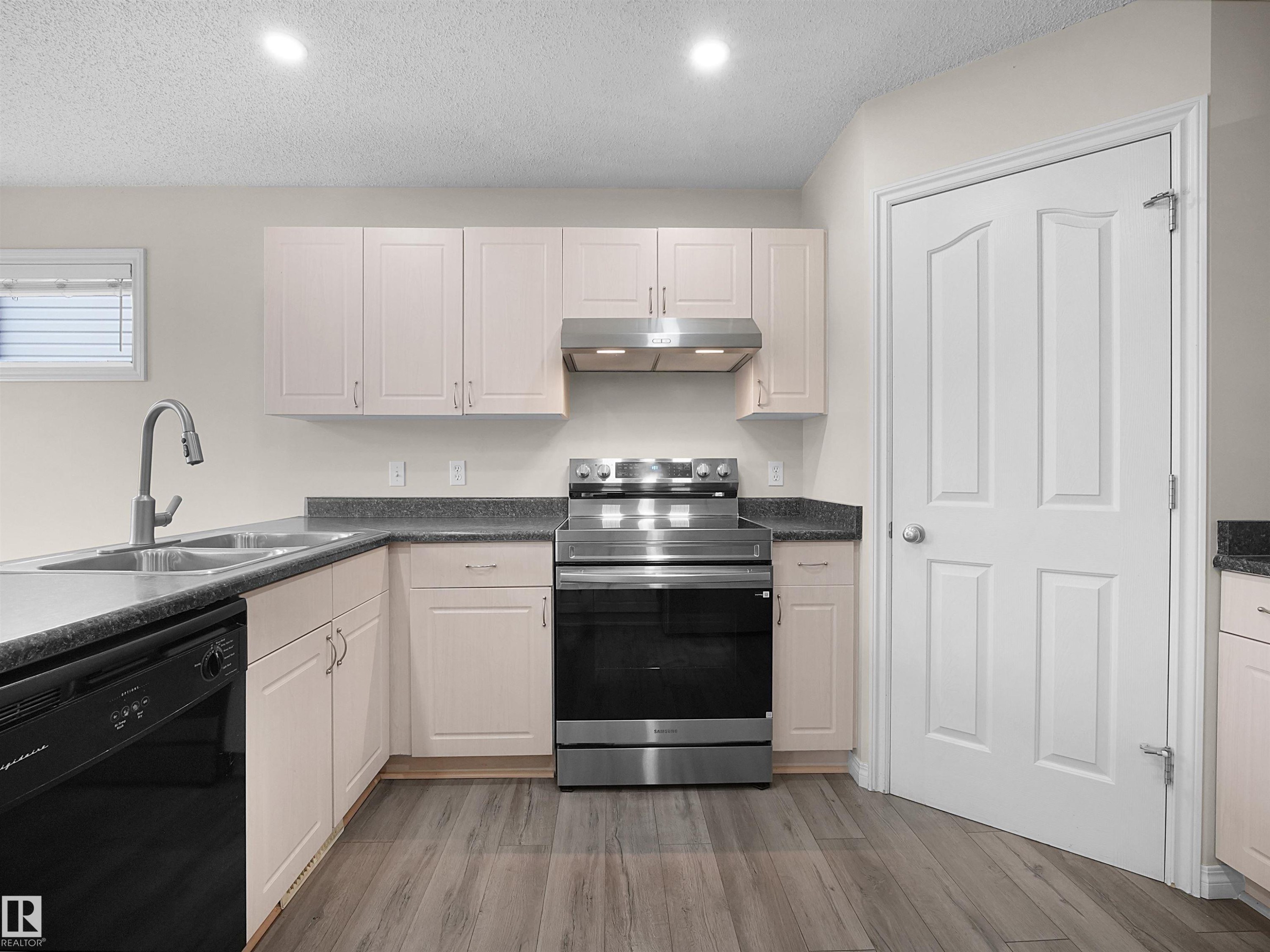 Modern kitchen featuring light-toned cabinetry, dark countertops, a stainless steel range with matching hood, a double basin sink with a gooseneck faucet, and wood-finish flooring - 7407 Singer Landing, Edmonton, AB - Indoor Photo Showing Kitchen With Double Sink