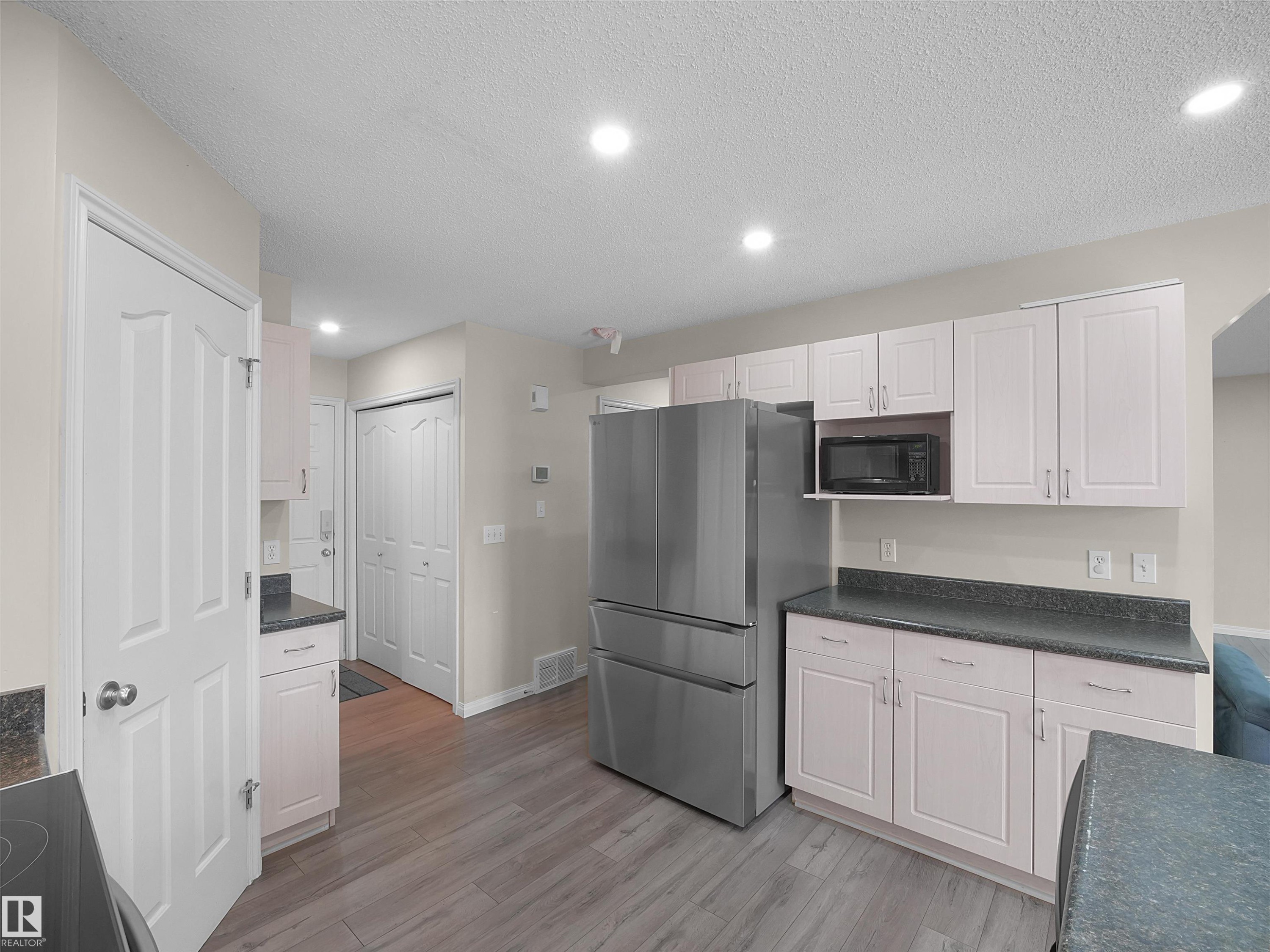 Kitchen featuring wood-finish flooring, recessed lighting, white cabinetry, dark countertops, and stainless steel appliances - 7407 Singer Landing, Edmonton, AB - Indoor