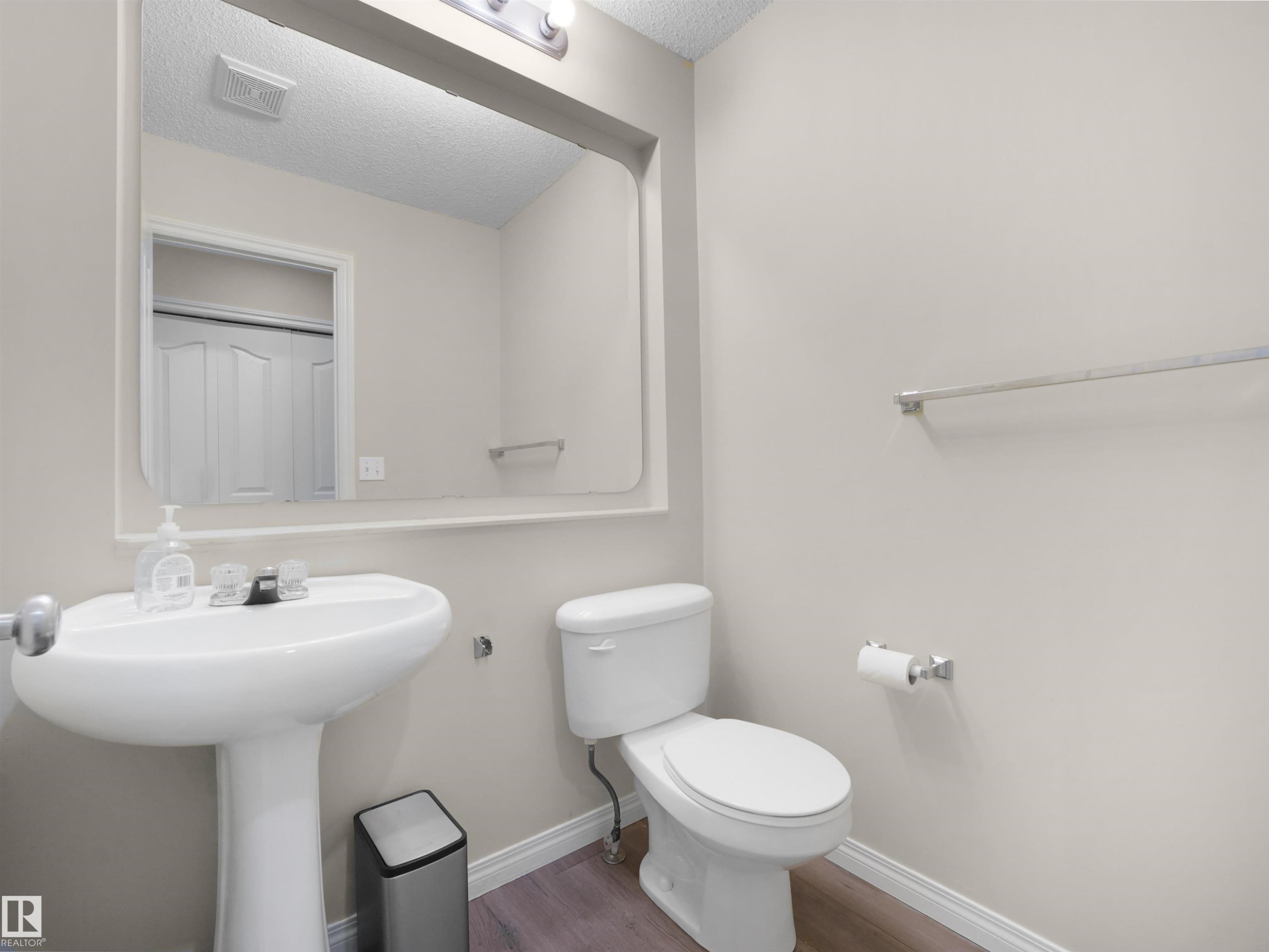 Powder room featuring a pedestal sink, white toilet, and wood-finish flooring - 7407 Singer Landing, Edmonton, AB - Indoor Photo Showing Bathroom