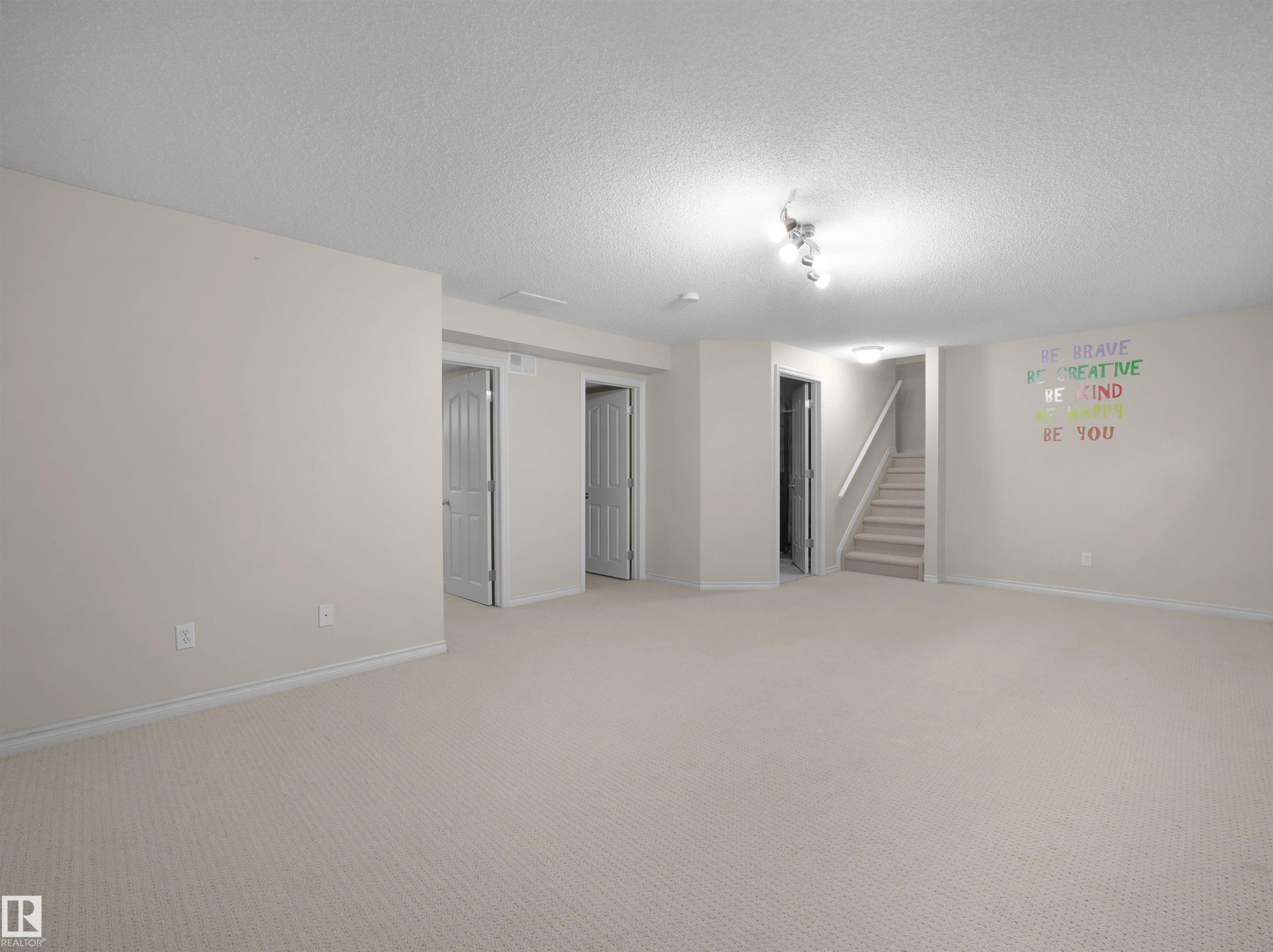 Expansive carpeted room featuring multiple closed doors and a staircase with a white handrail - 7407 Singer Landing, Edmonton, AB - Indoor Photo Showing Other Room