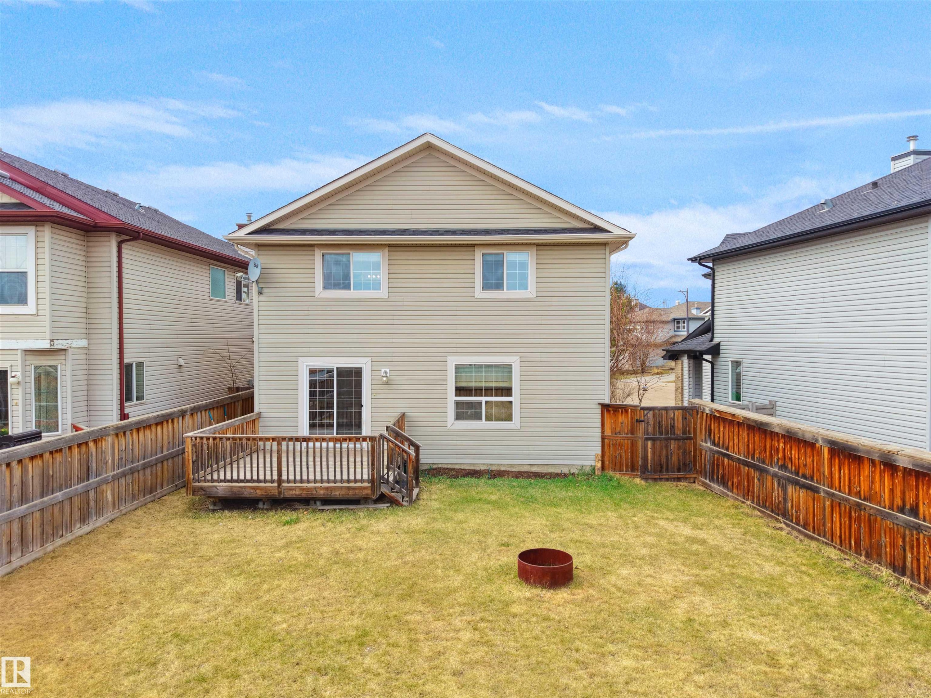 Rear exterior featuring light-colored siding, a wooden deck, sliding glass patio door, and a fenced backyard - 7407 Singer Landing, Edmonton, AB - Outdoor With Deck Patio Veranda With Exterior
