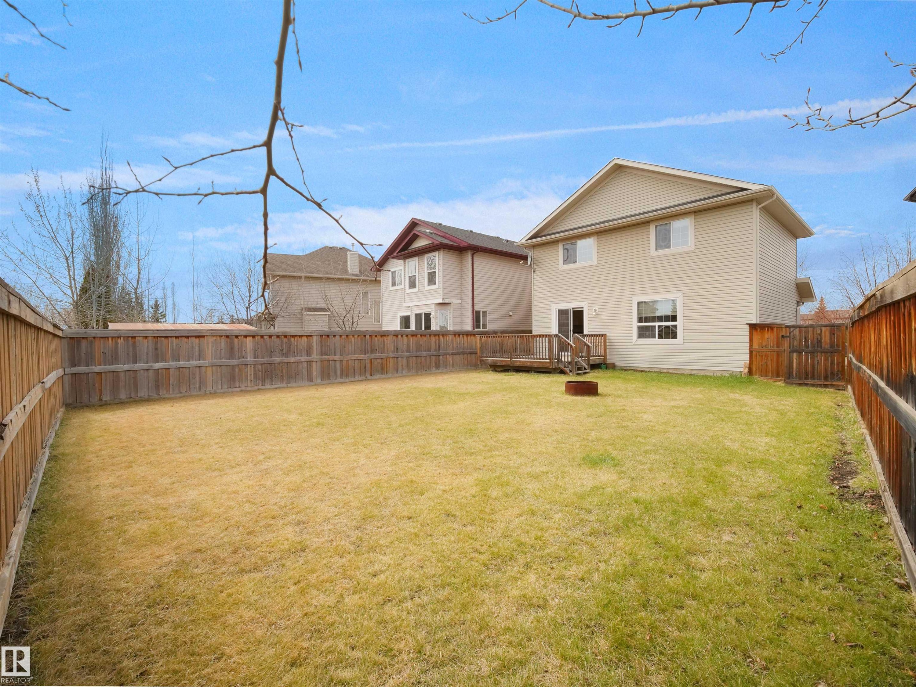 Expansive backyard featuring a large grass area, wood privacy fencing, and a rear deck with direct home access - 7407 Singer Landing, Edmonton, AB - Outdoor