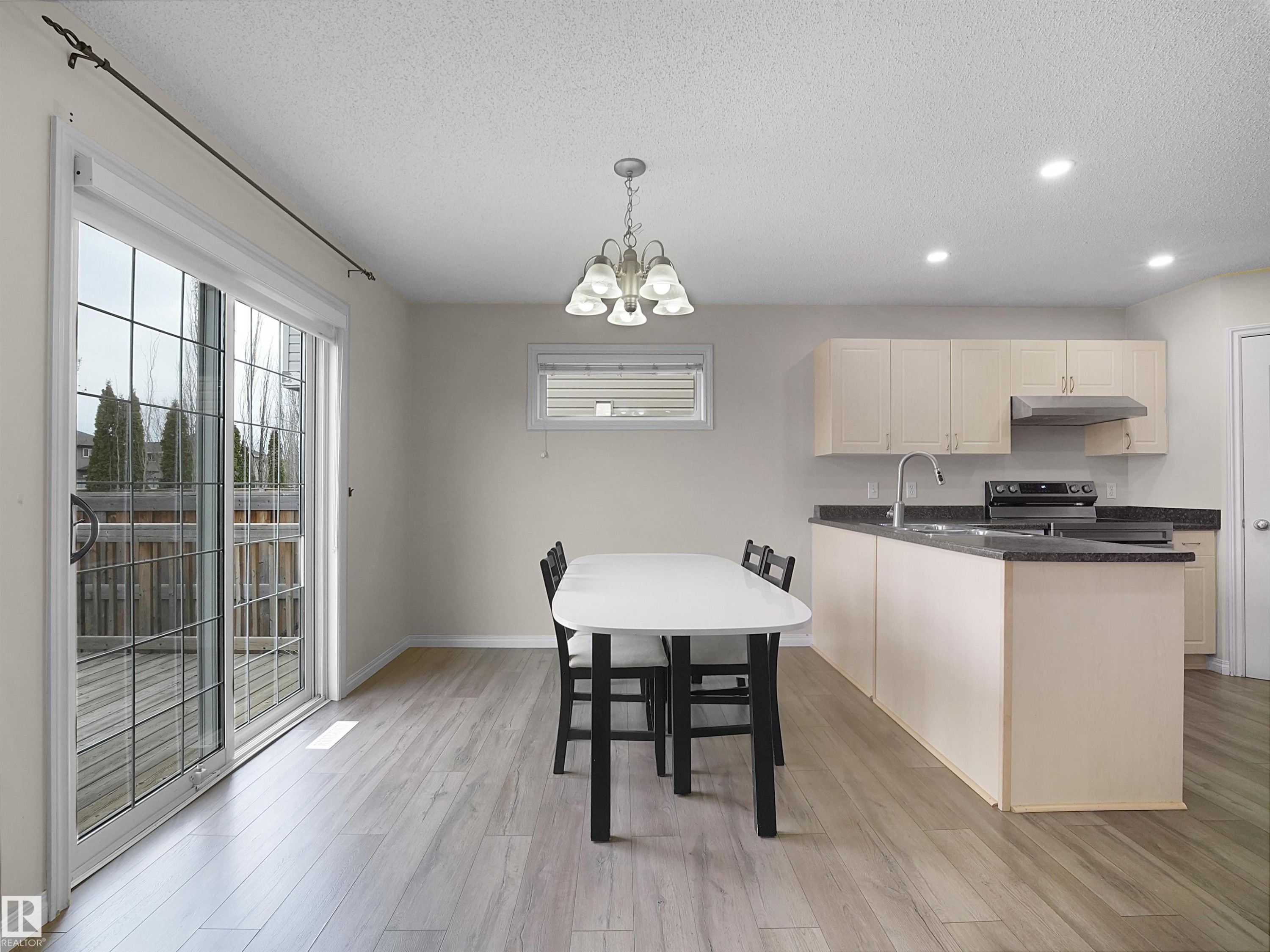 Open-concept kitchen and dining area featuring light-toned cabinetry, dark countertops, and stainless steel appliances - 7407 Singer Landing, Edmonton, AB - Indoor